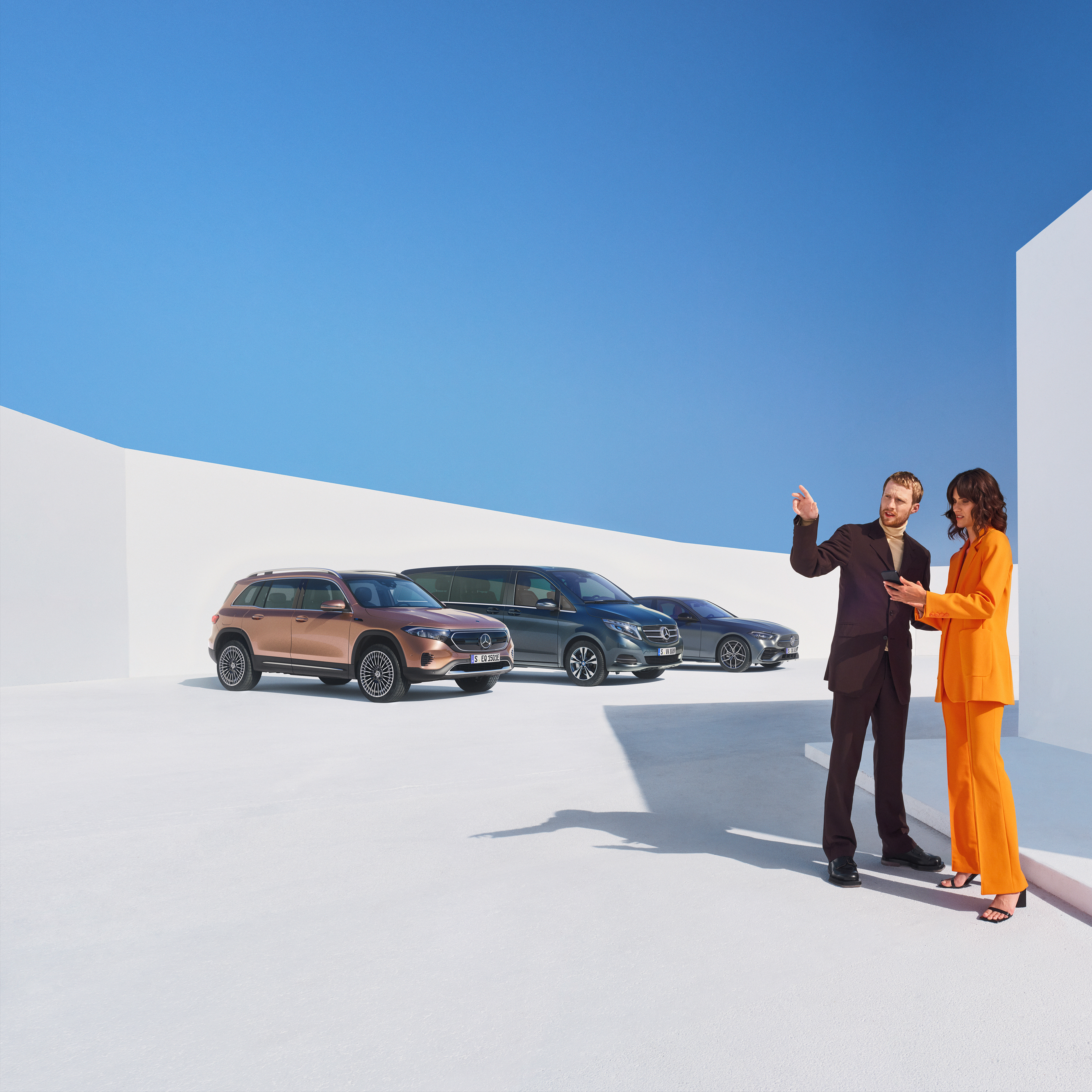 Business | Digital Extras Due persone parlano davanti a tre veicoli Mercedes-Benz.