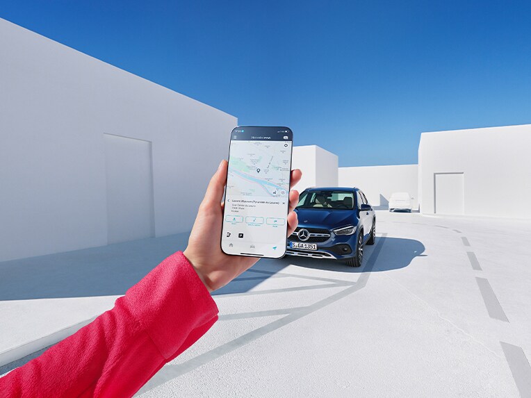 Jemand hält ein Handy in der Hand, auf dem man die Mercedes-Benz Service App sieht. Im Hintergrund steht ein Mercedes-Benz Fahrzeug.