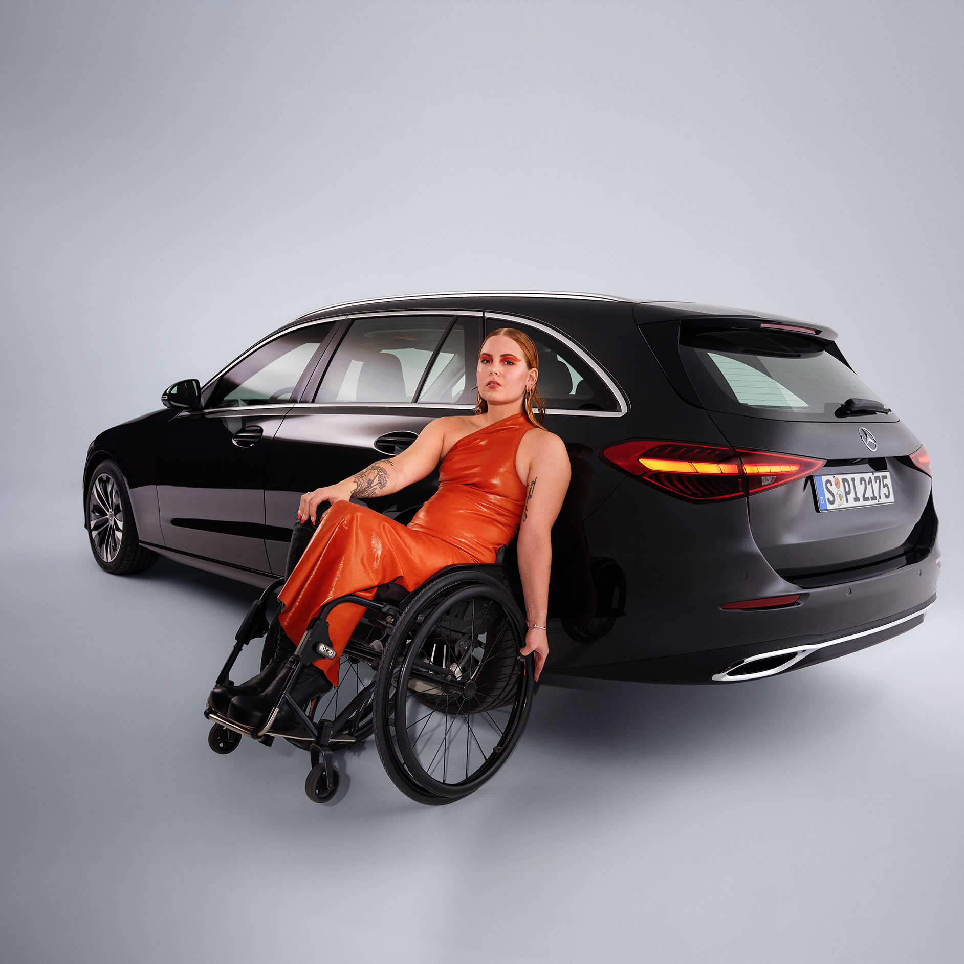 Qualité | Aides à la conduite | Mercedes-Benz Un véhicule adapté aux personnes à mobilité réduite : la Classe C Break dans une vue de 3/4 arrière et une femme en fauteuil roulant.