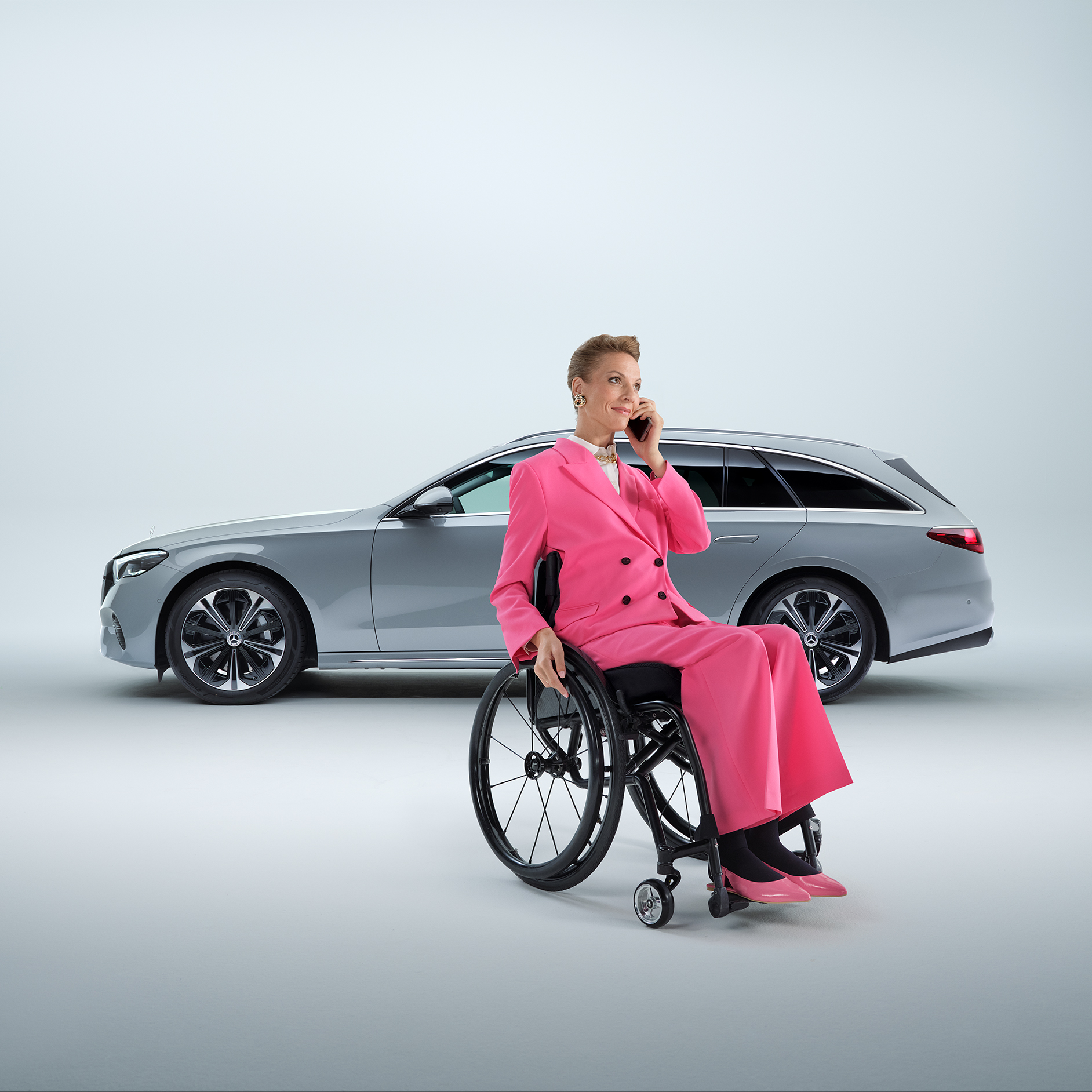 Conseils | Aides à la conduite | Mercedes-Benz Vue latérale d'un break Mercedes-Benz Classe E transformé en voiture pour personnes à mobilité réduite, avec au premier plan une femme en fauteuil roulant tenant un smartphone.