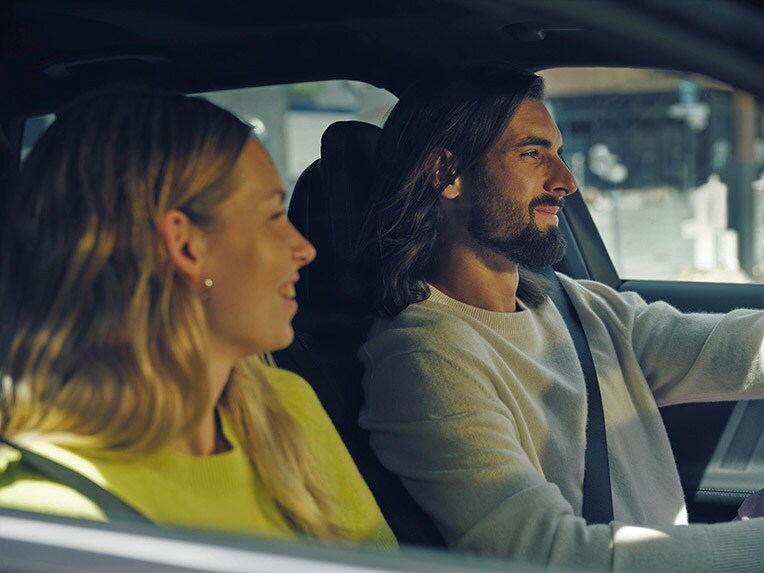 Mann sitzt in einem Mercedes-Benz und zeigt einer Frau, die draußen steht, sein Mobiltelefon