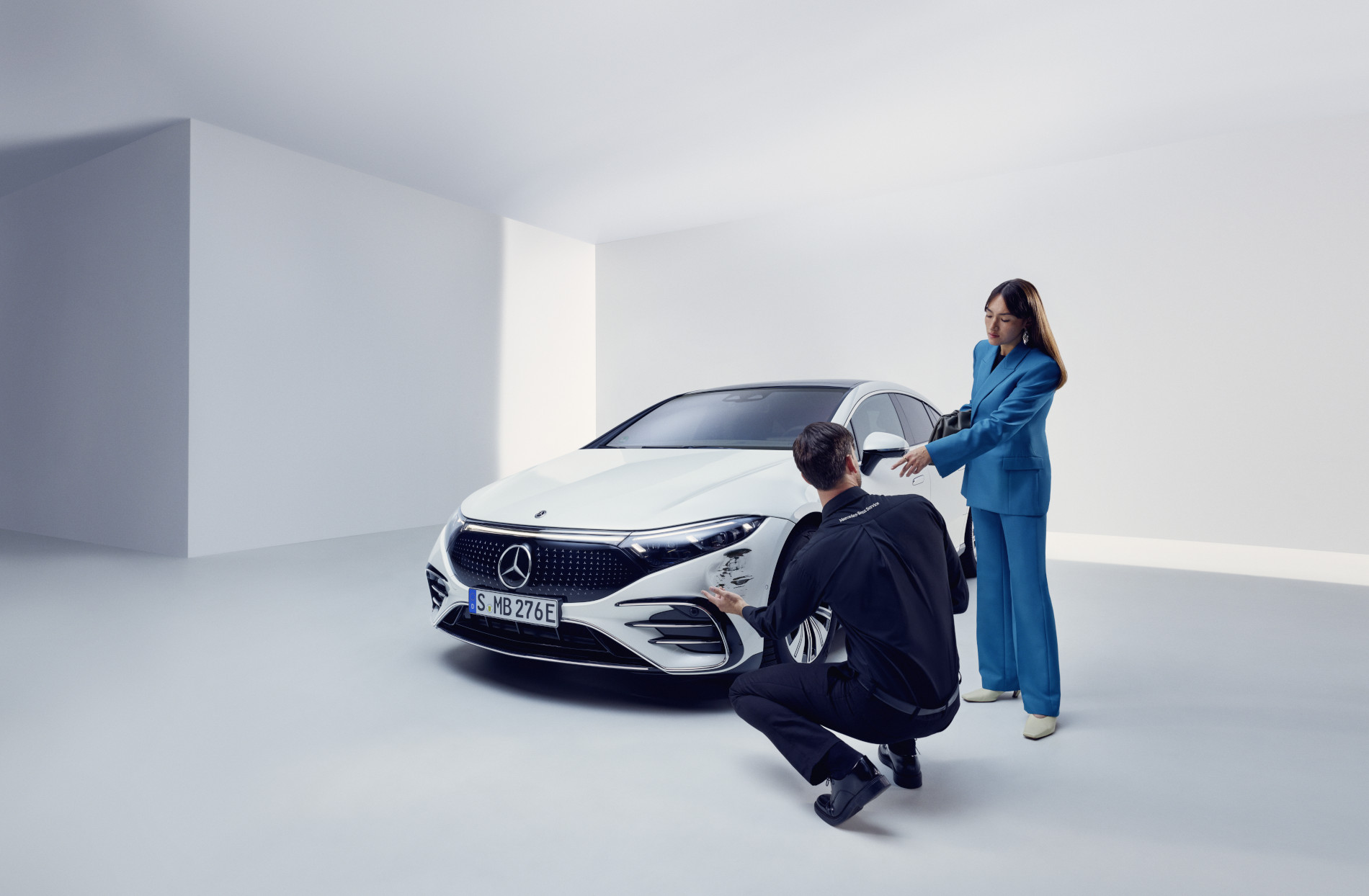 Réparation des dommages | Mercedes-Benz Une personne de l'équipe d'assistance Mercedes-Benz agenouillée près d'une Mercedes-Benz endommagée.