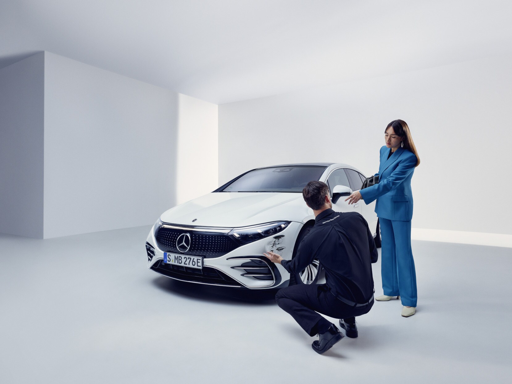 Una persona del servizio assistenza Mercedes-Benz inginocchiato accanto a una Mercedes-Benz danneggiata.