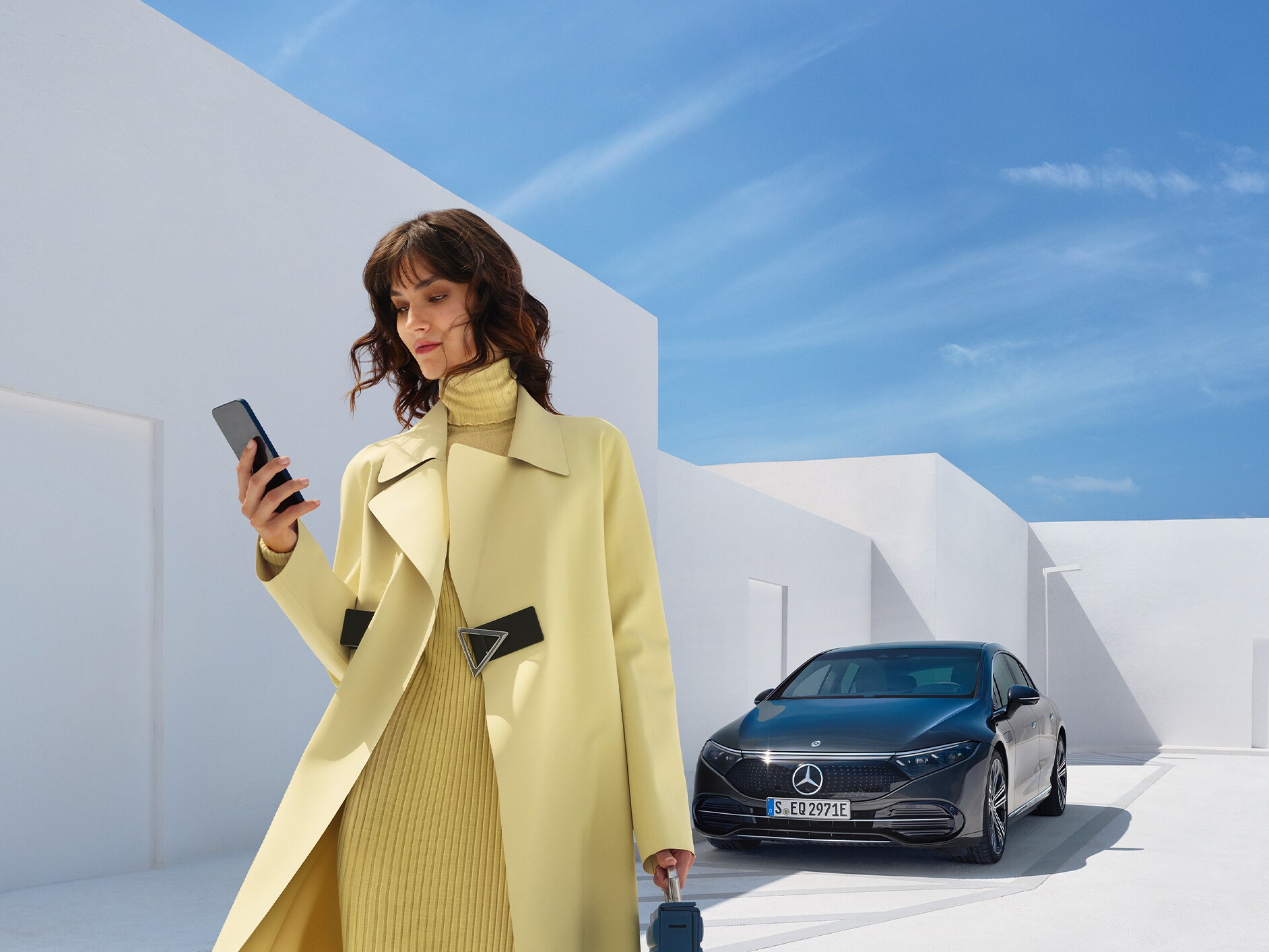 Una donna guarda il cellulare mentre si allontana dalla sua Mercedes-Benz con tecnologia EQ.