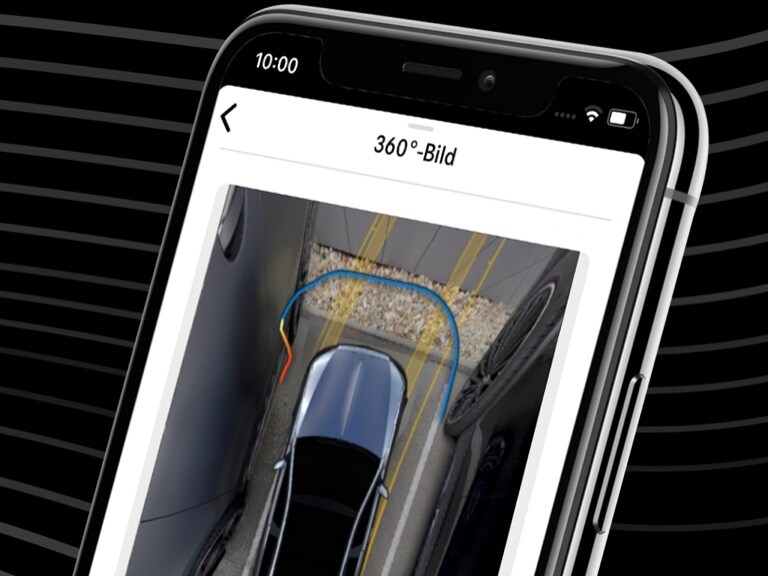 Ein Mercedes-Benz wird per Mercedes me Remote Park-Assistent App und der 360°-Ansicht auf einem Smartphone bequem in eine enge Parklücke gesteuert.