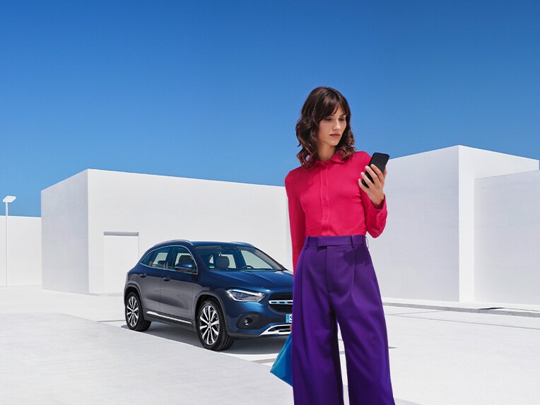 Eine Frau nutzt die Mercedes-Benz Service App auf ihrem Smartphone, um sich mit Ihrem Mercedes-Benz zu verbinden.