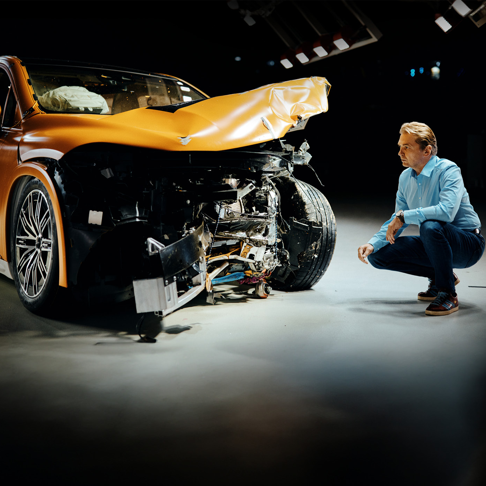 Crashtest-Experten | Sicherheit | Mercedes-Benz Crashtest-Experte bei der Untersuchung eines frontal beschädigten Mercedes-Benz Fahrzeugs, während er daneben kauert.