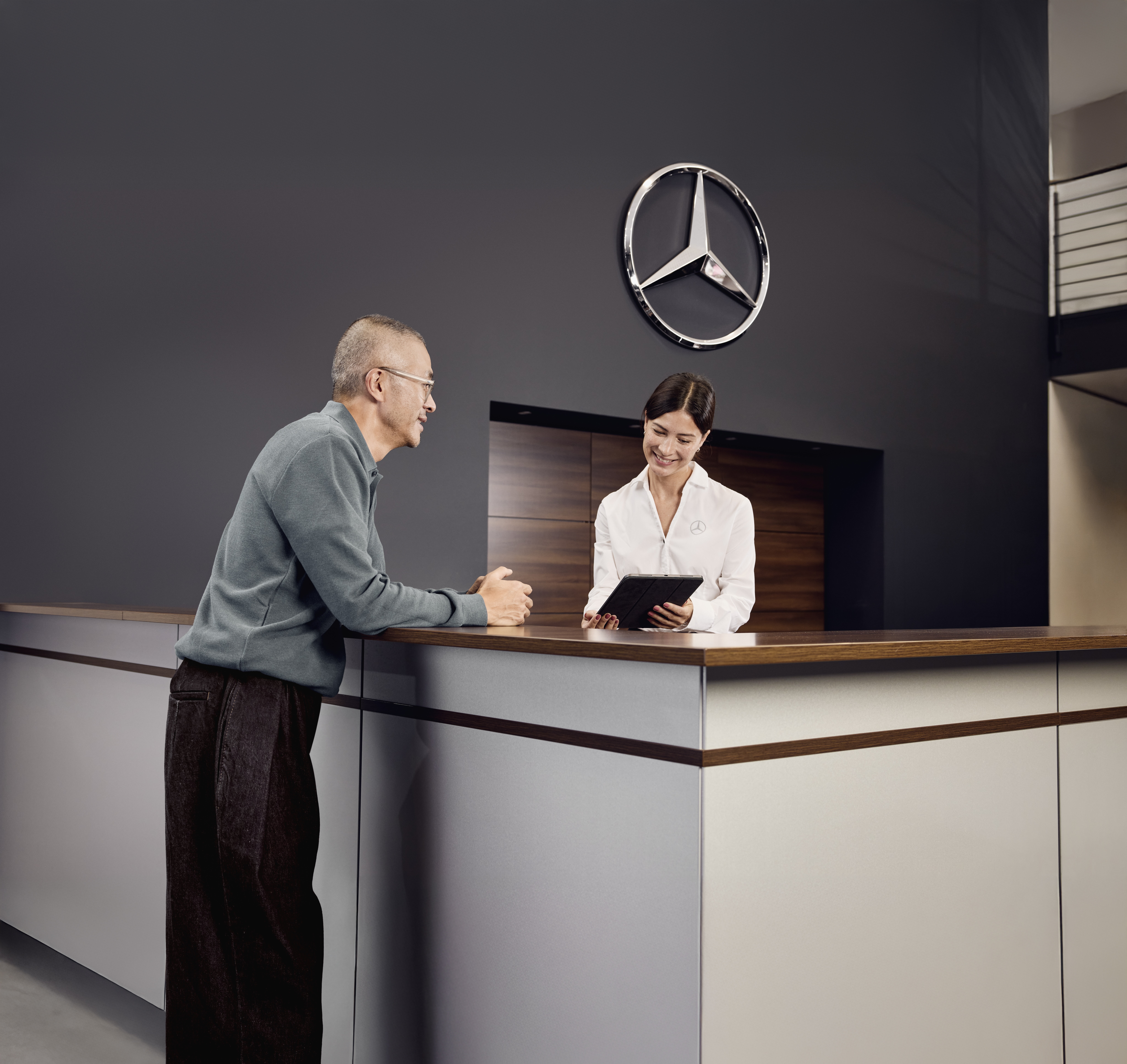 Conseils sur les pièces d'origine Mercedes-Benz Accueil du service après-vente d'un distributeur Mercedes-Benz, où un client discute des détails de la maintenance de son véhicule avec un conseiller du service après-vente.