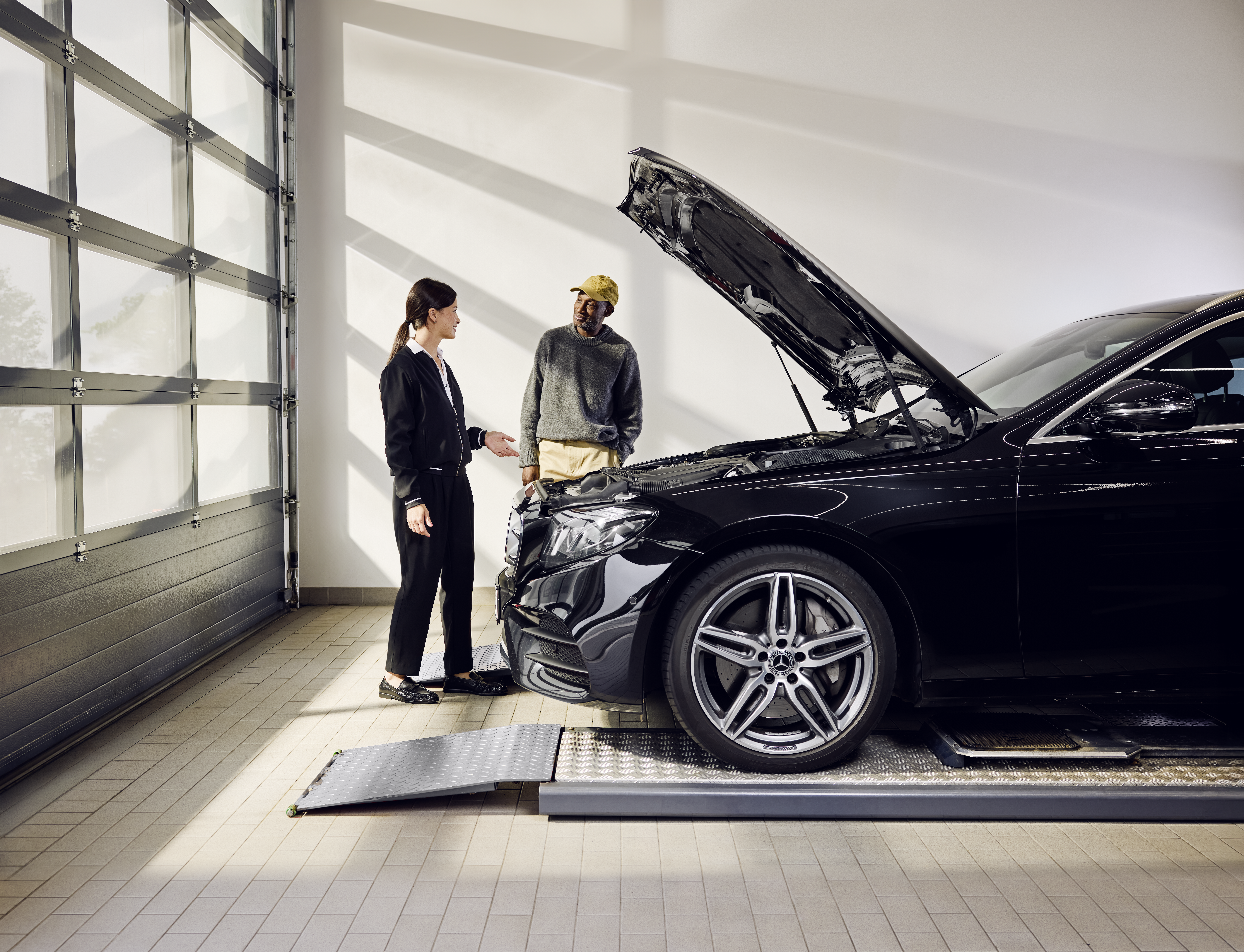 Remplacement des pièces d'origine Mercedes-Benz Véhicule Mercedes-Benz placé sur une rampe de service, le capot moteur ouvert, lors d'un remplacement professionnel de pièces d'origine dans un point de service.