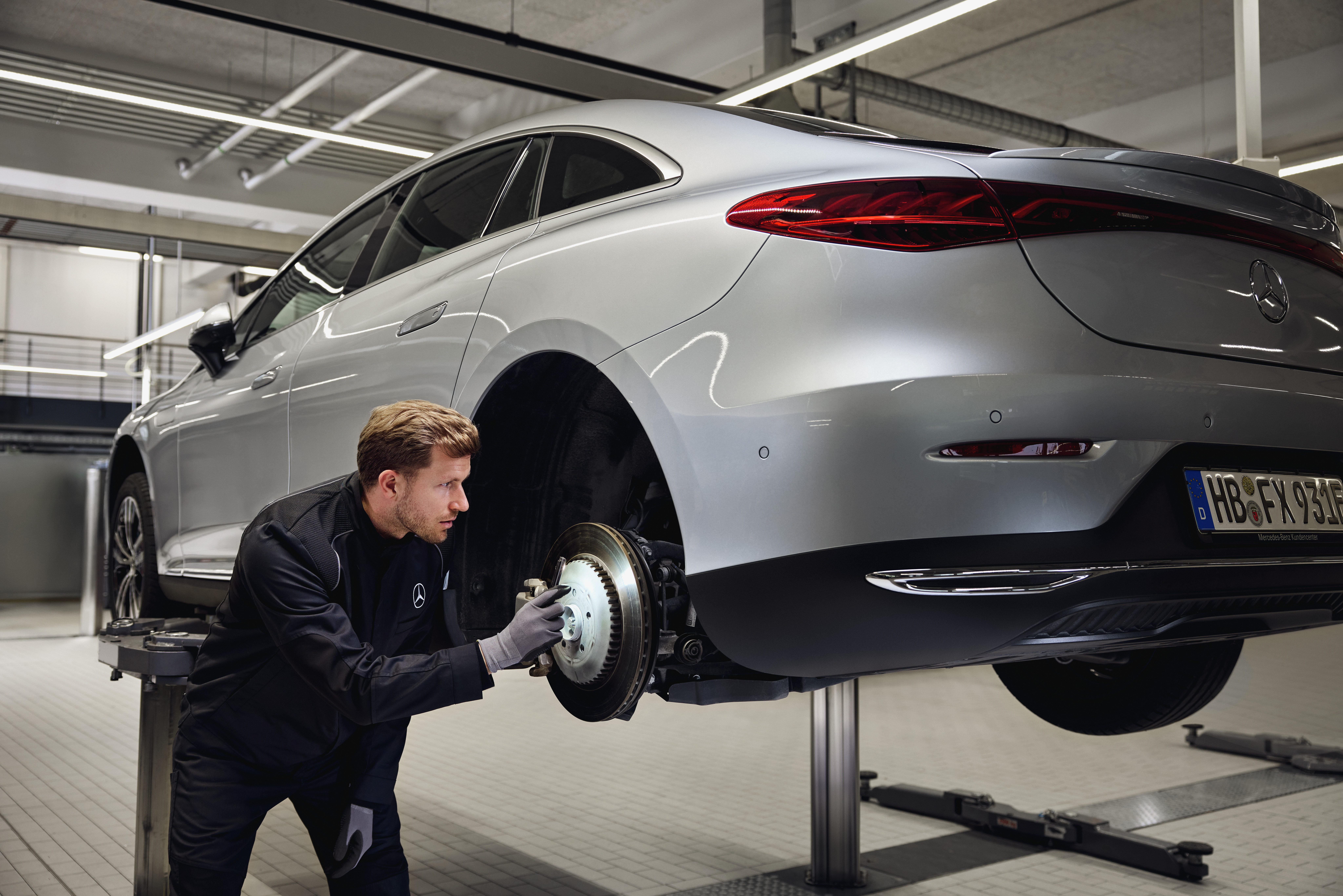 Original-Bremsenersatz von Mercedes-Benz Ein Mercedes-Benz-Fahrzeug steht auf einer Hebebühne, während ein Techniker die hintere Bremsanlage im Rahmen eines Austauschs von Originalteilen überprüft.