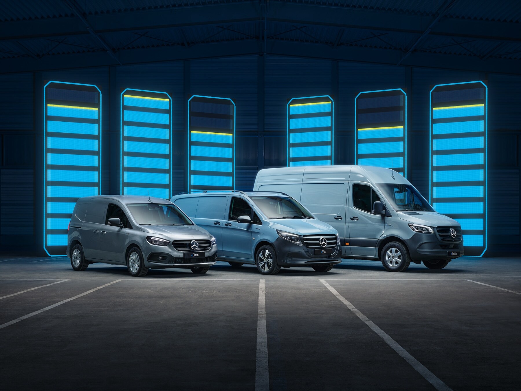 La gamme d'utilitaires légers électriques Mercedes-Benz exposée dans un entrepôt au design futuriste, avec des bornes de recharge lumineuses