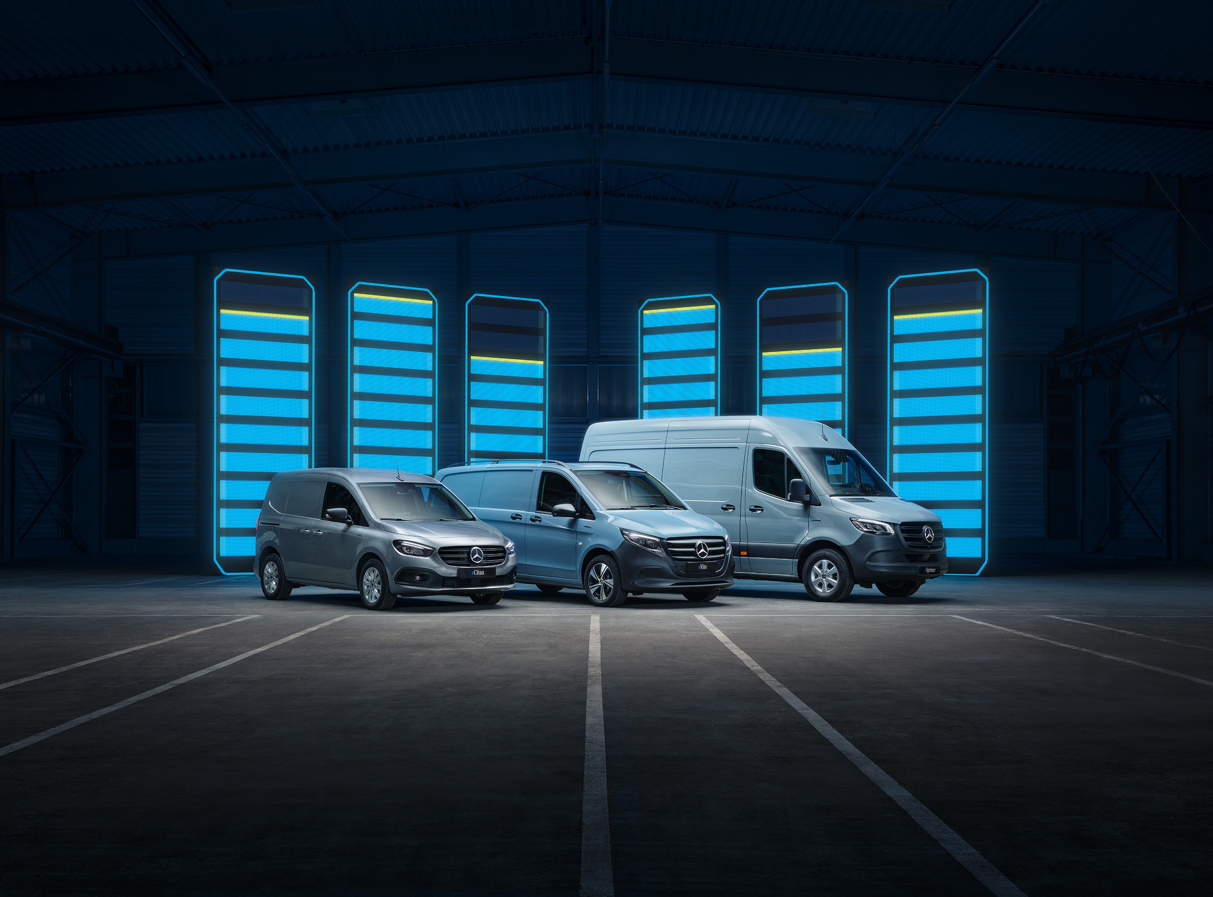 Gamme d'utilitaires légers électriques Mercedes-Benz | Histoire des véhicules industriels | Mercedes-Benz La gamme d'utilitaires légers électriques Mercedes-Benz exposée dans un entrepôt au design futuriste, avec des bornes de recharge lumineuses