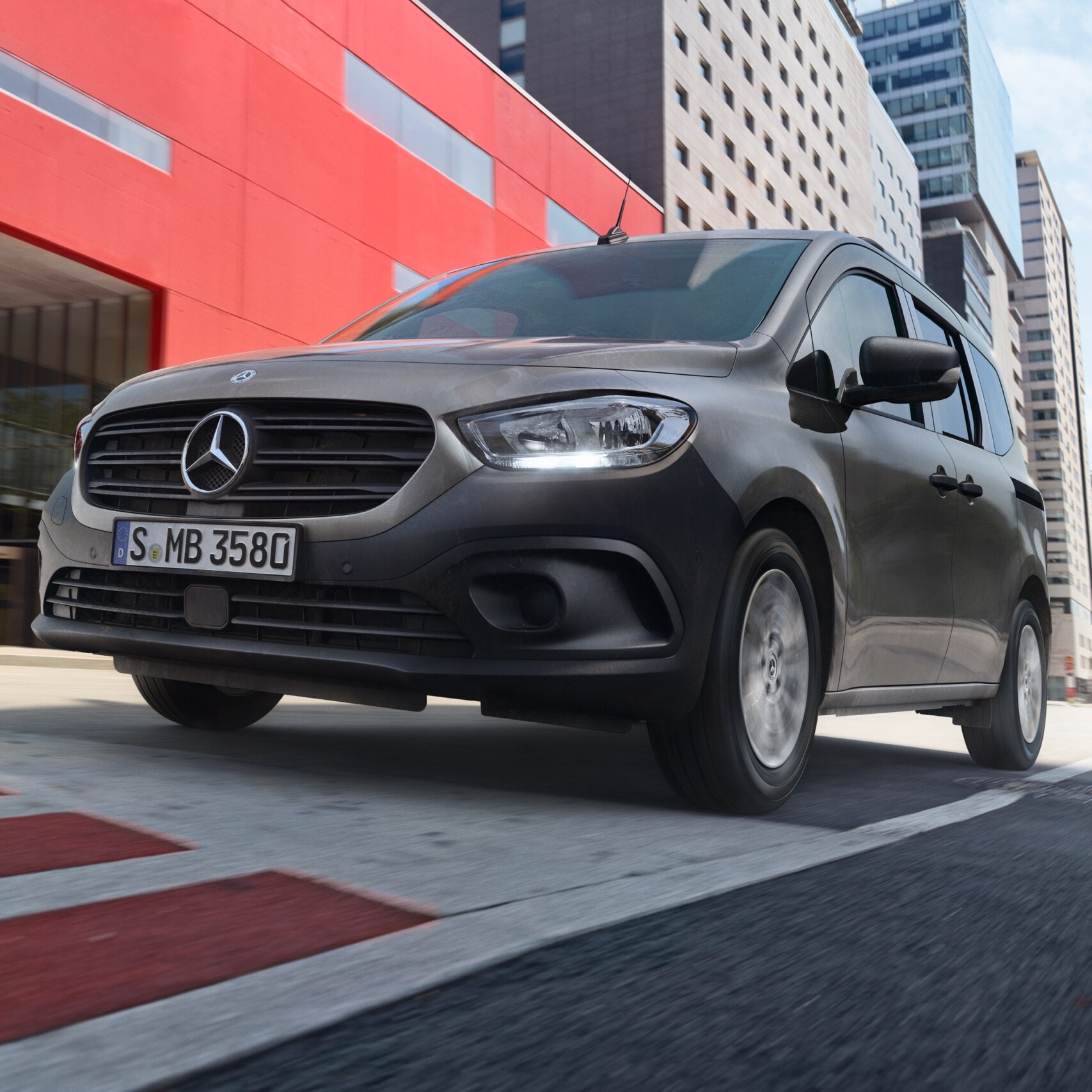 Il Citan Tourer, un furgone per il trasporto passeggeri Mercedes-Benz, passa attraverso un quartiere urbano moderno.
