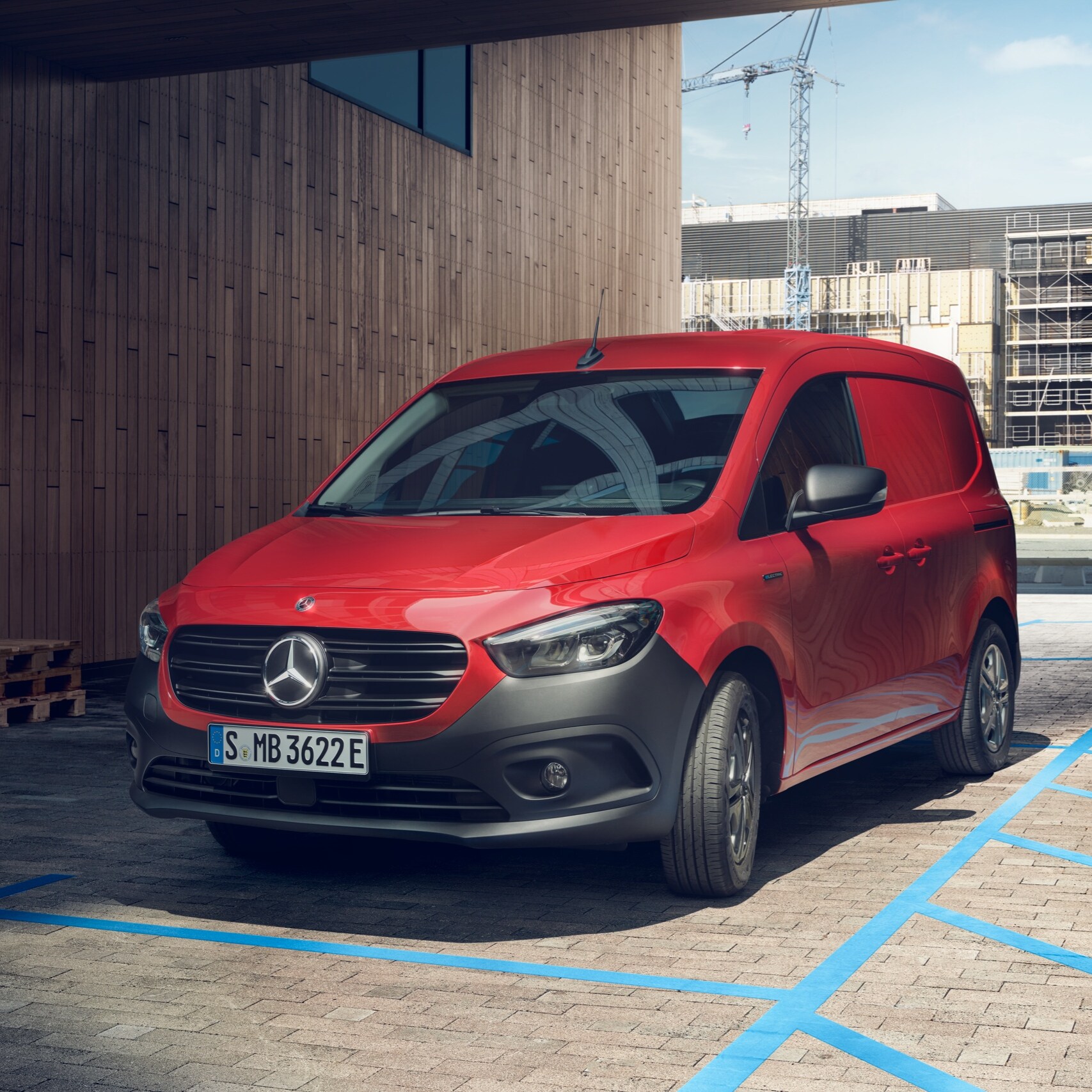 L'eCitan Furgone, un veicolo commerciale elettrico Mercedes-Benz, parcheggiato a una stazione di ricarica davanti a un edificio moderno.