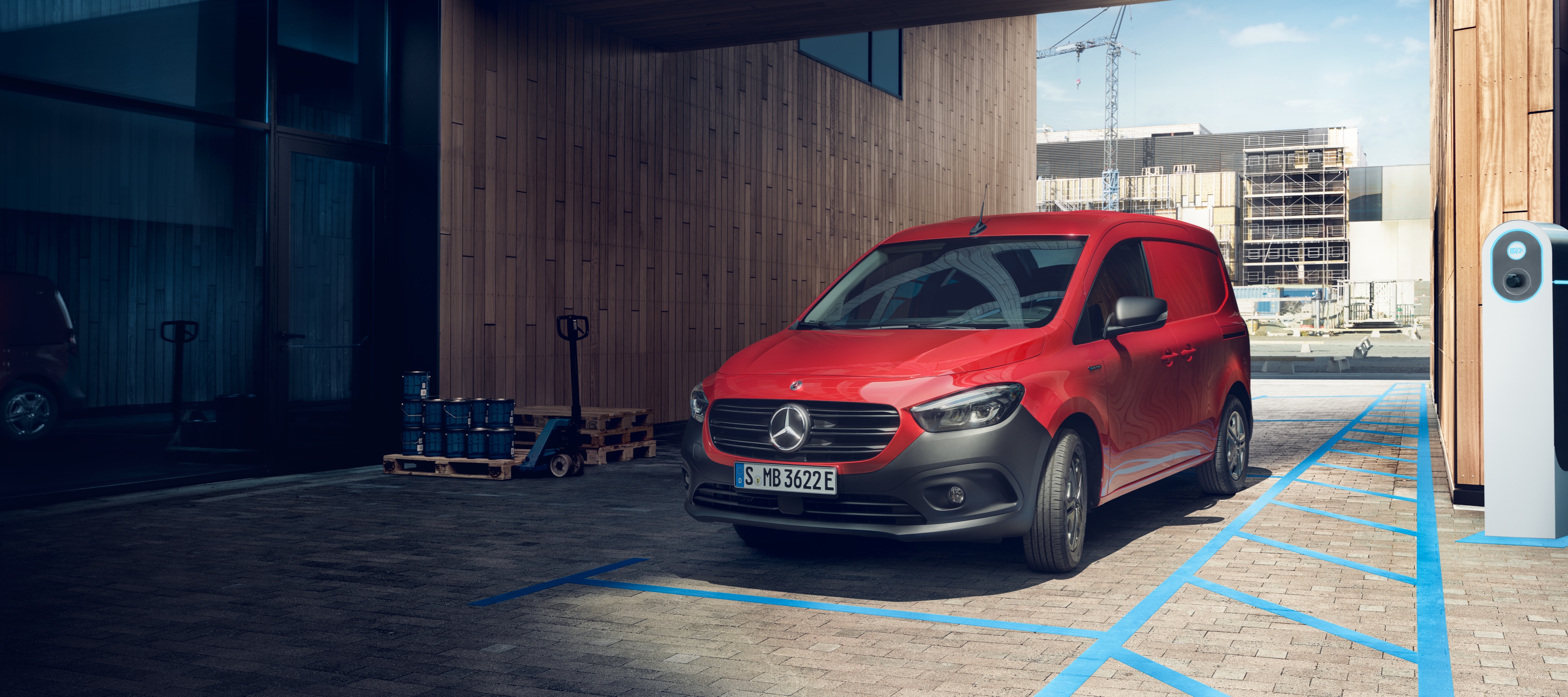 eCitan Furgone | Veicoli commerciali Mercedes-Benz L'eCitan Furgone, un veicolo commerciale elettrico Mercedes-Benz, parcheggiato a una stazione di ricarica davanti a un edificio moderno.