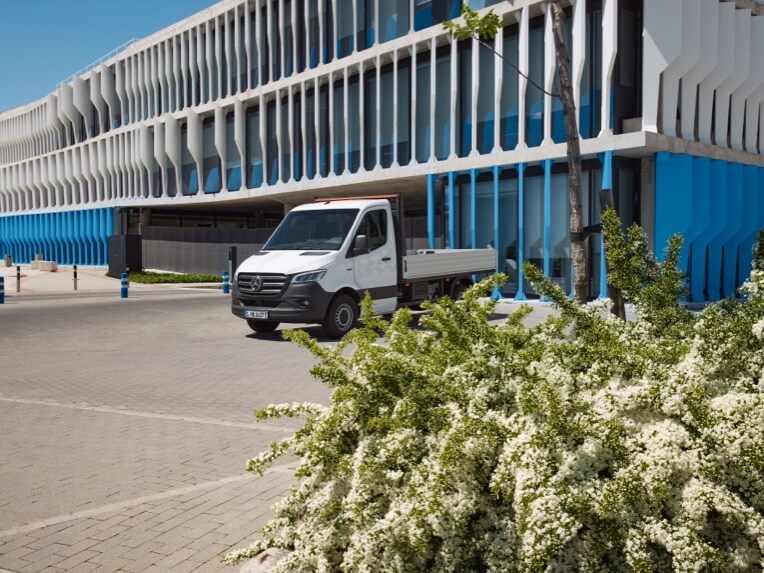 Das Mercedes-Benz eSprinter Fahrgestell als Pritschenfahrzeug parkt vor einem Gebäude.