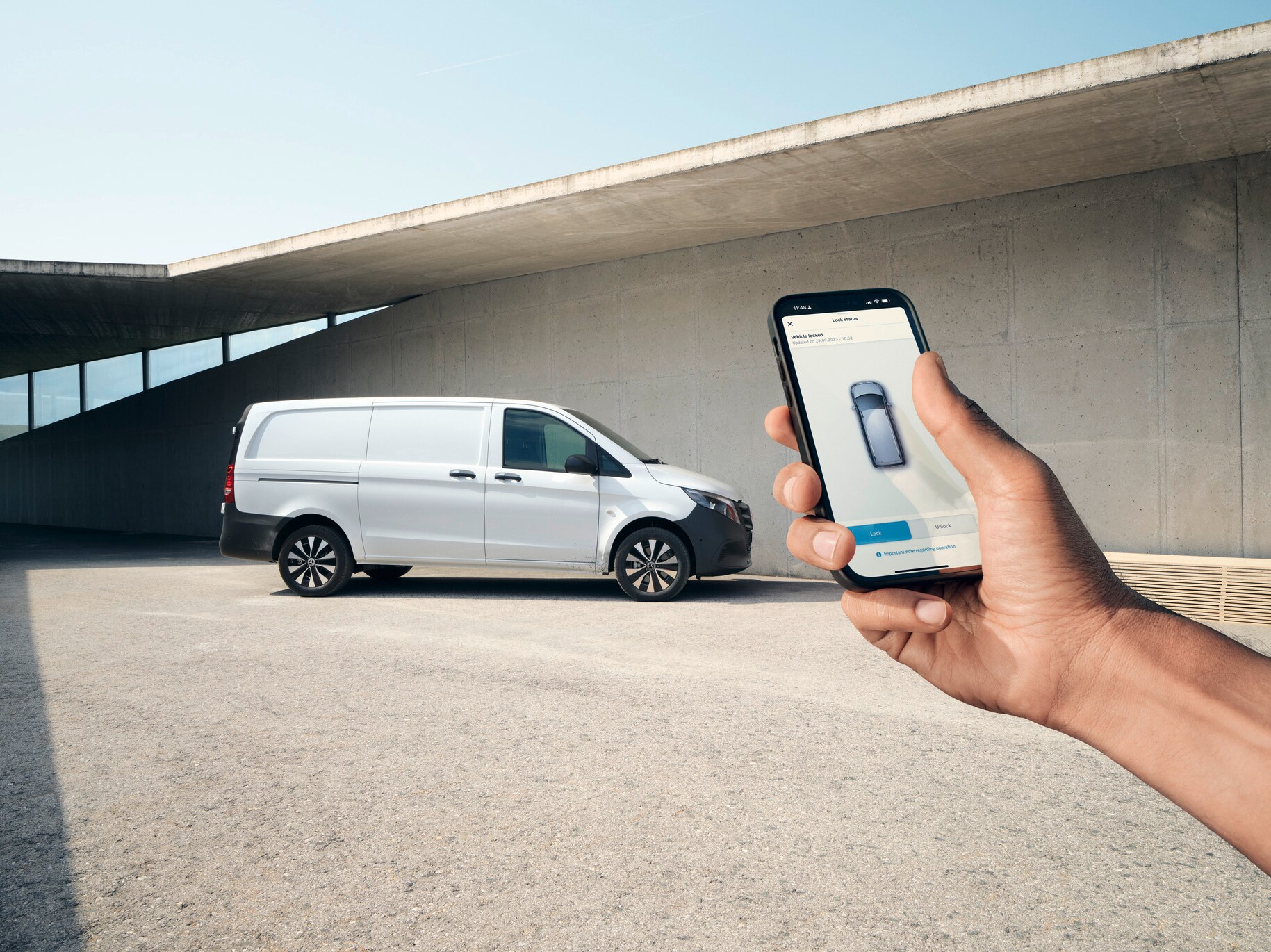 Main tenant un smartphone montrant l'application Mercedes me. Vito fourgon en arrière-plan.