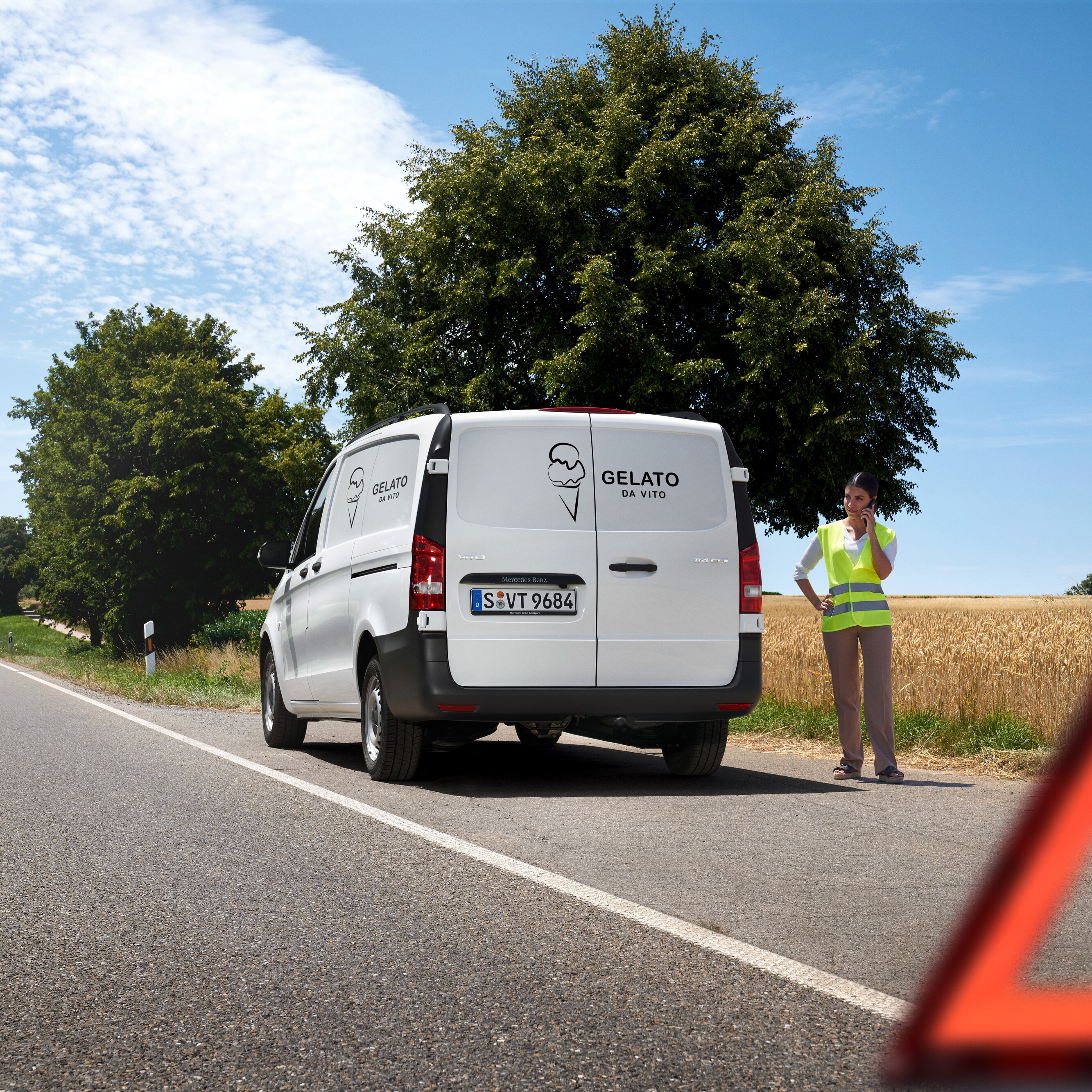 A woman calls the Mercedes-Benz service 24h hotline, a Mercedes-Benz Sprinter is stationary by the side of country road.