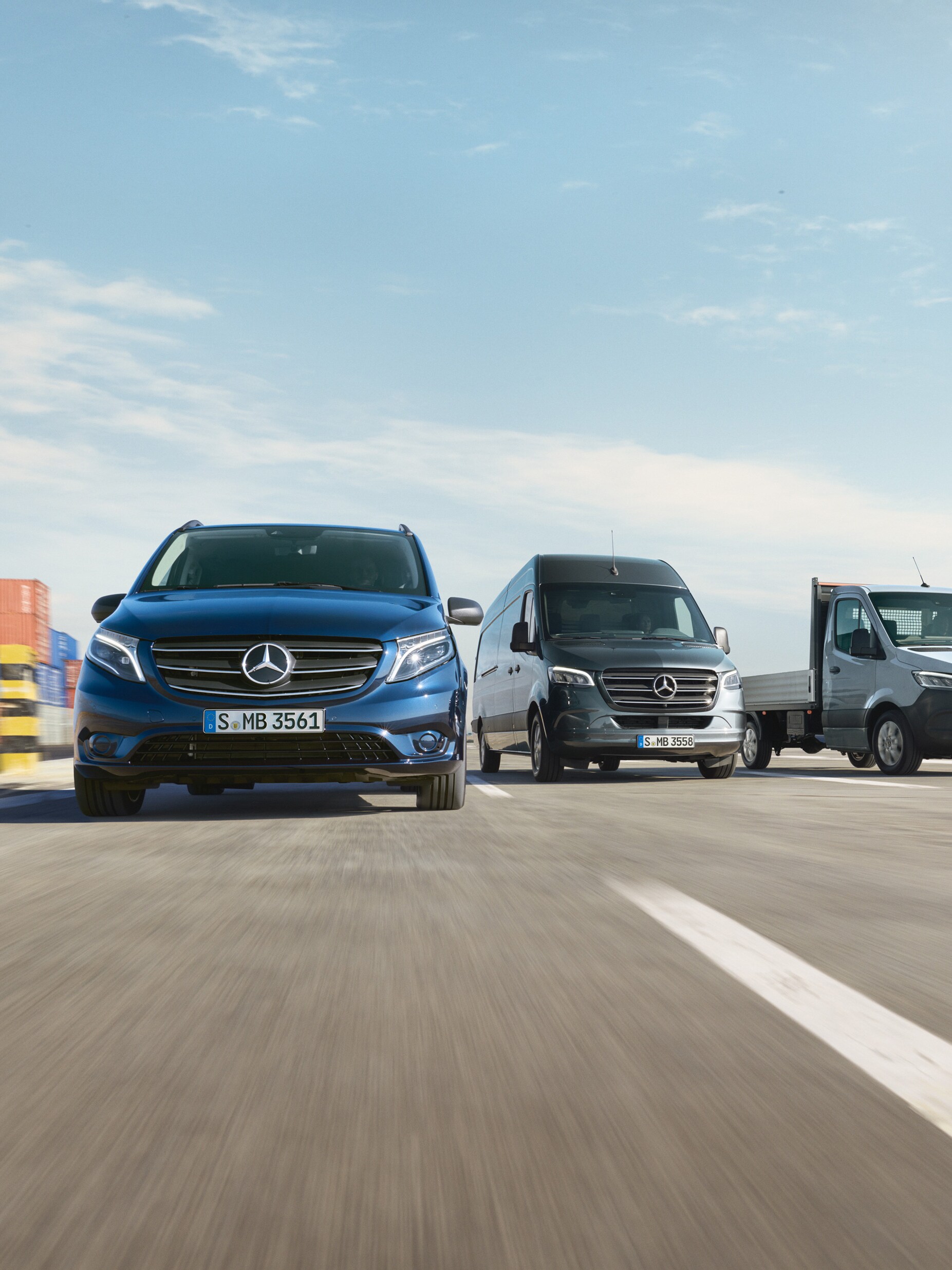Una serie di veicoli commerciali Mercedes-Benz parcheggiati uno accanto all'altro su una strada accanto a un molo di spedizione.