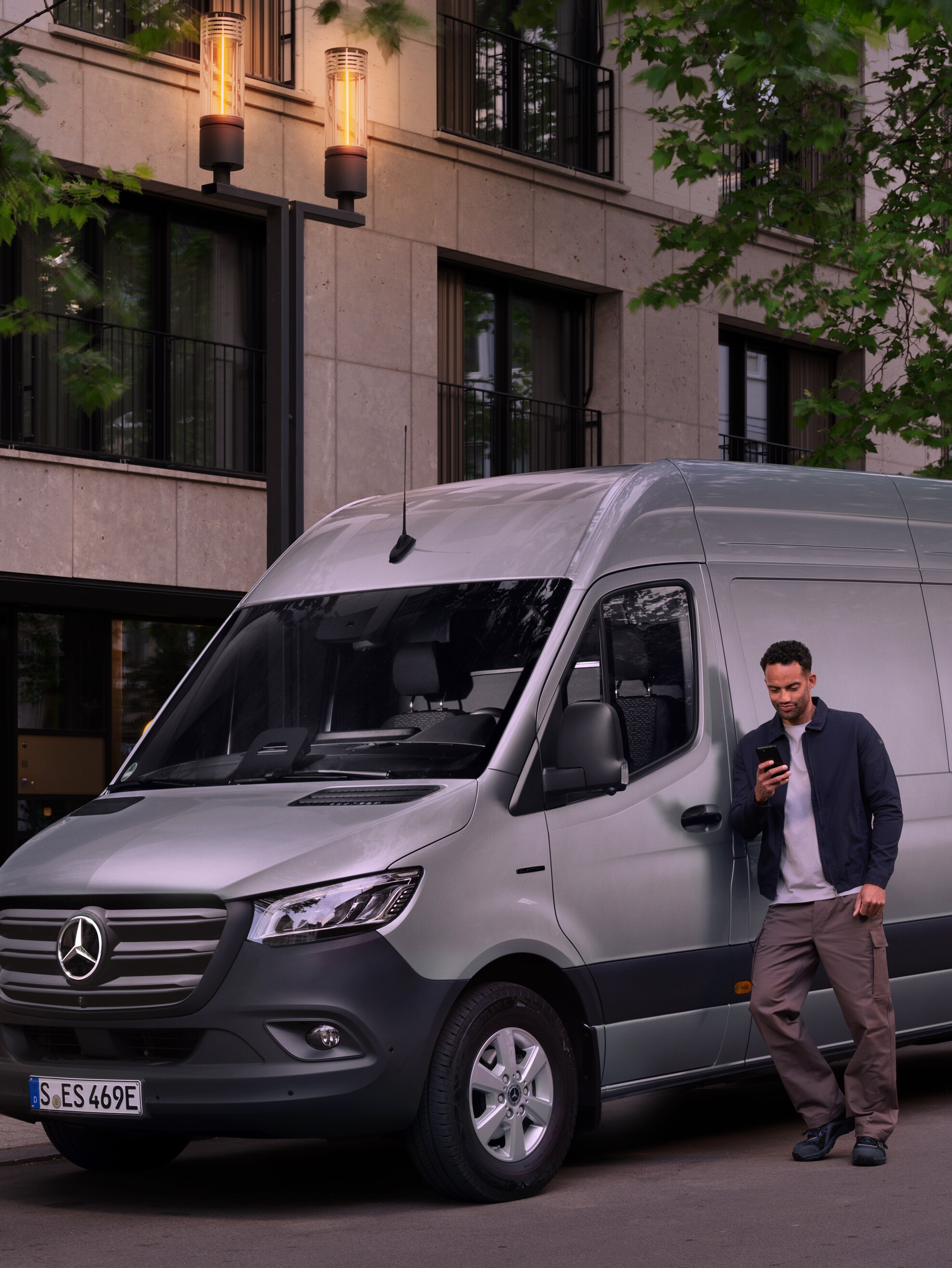 Un homme s'appuie sur un utilitaire léger Mercedes-Benz Sprinter argenté et utilise son smartphone - assistance rapide du service clientèle de Mercedes Benz.