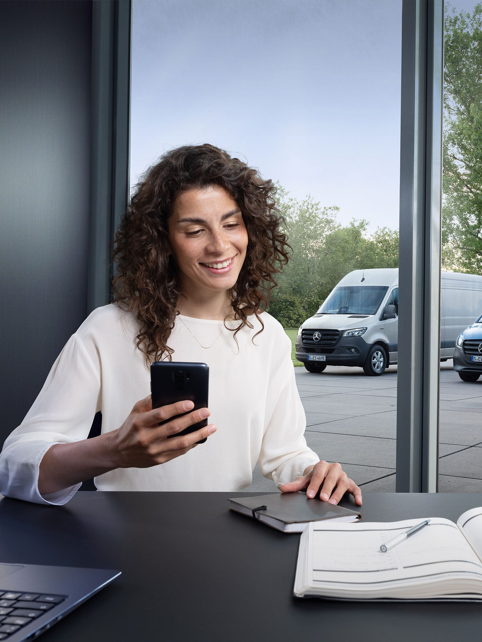 Femme avec smartphone devant des utilitaires Mercedes-Benz.