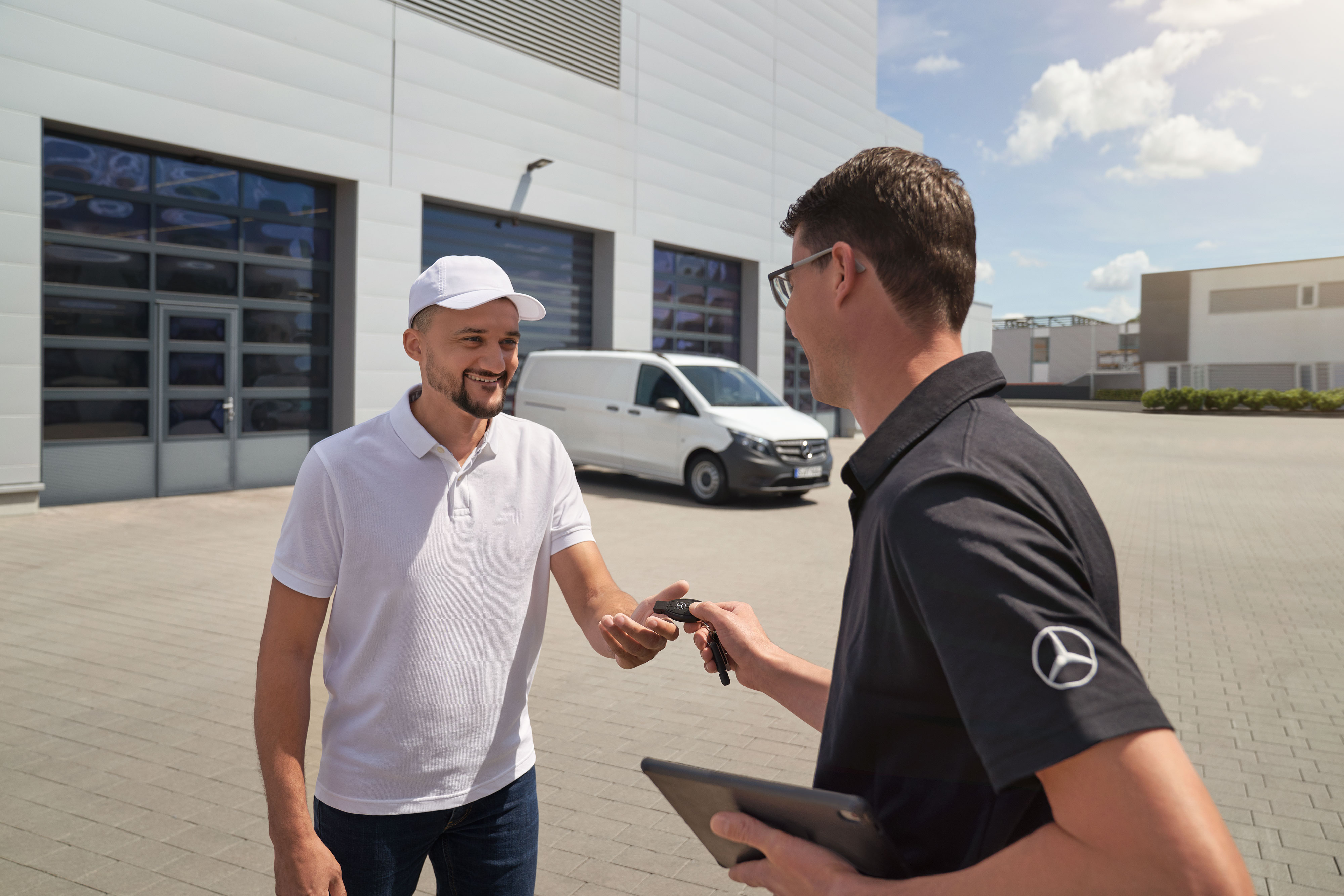 Mercedes-Benz | Convenience | Servizio di ritiro e consegna Un tecnico Mercedes-Benz consegna le chiavi a un cliente con un veicolo commerciale Mercedes-Benz Vito bianco sullo sfondo.