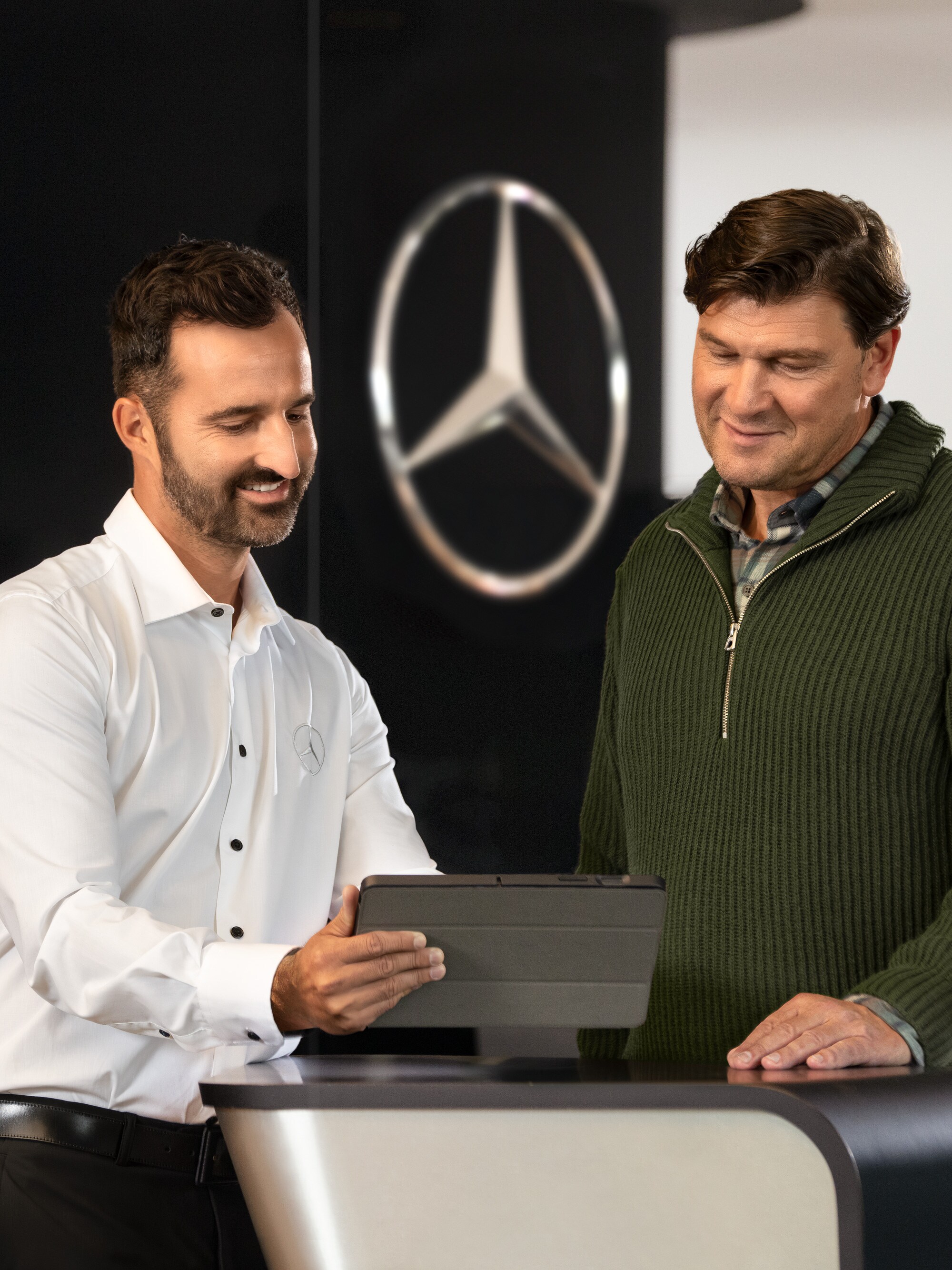 Un dipendente Mercedes-Benz parla con un cliente mentre guarda un dispositivo su un tavolo.
