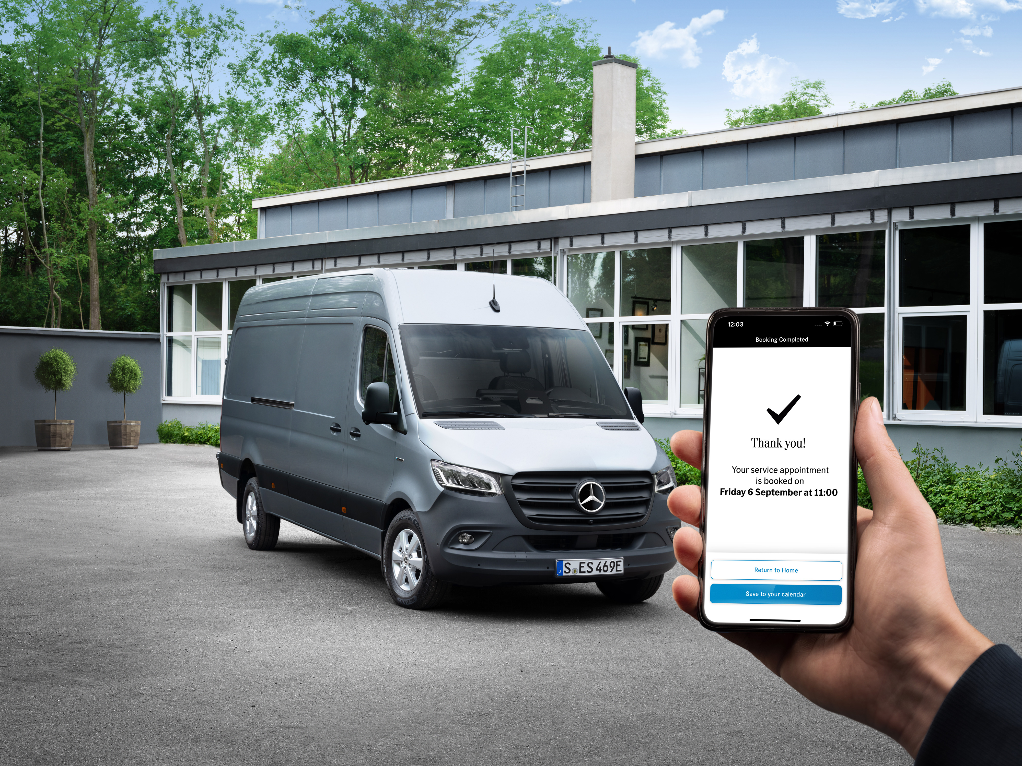 Mercedes-Benz | Convenience | Partner di assistenza Un veicolo commerciale Mercedes-Benz Sprinter grigio davanti a un ufficio, accanto una persona in primo piano che tiene in mano uno smartphone.