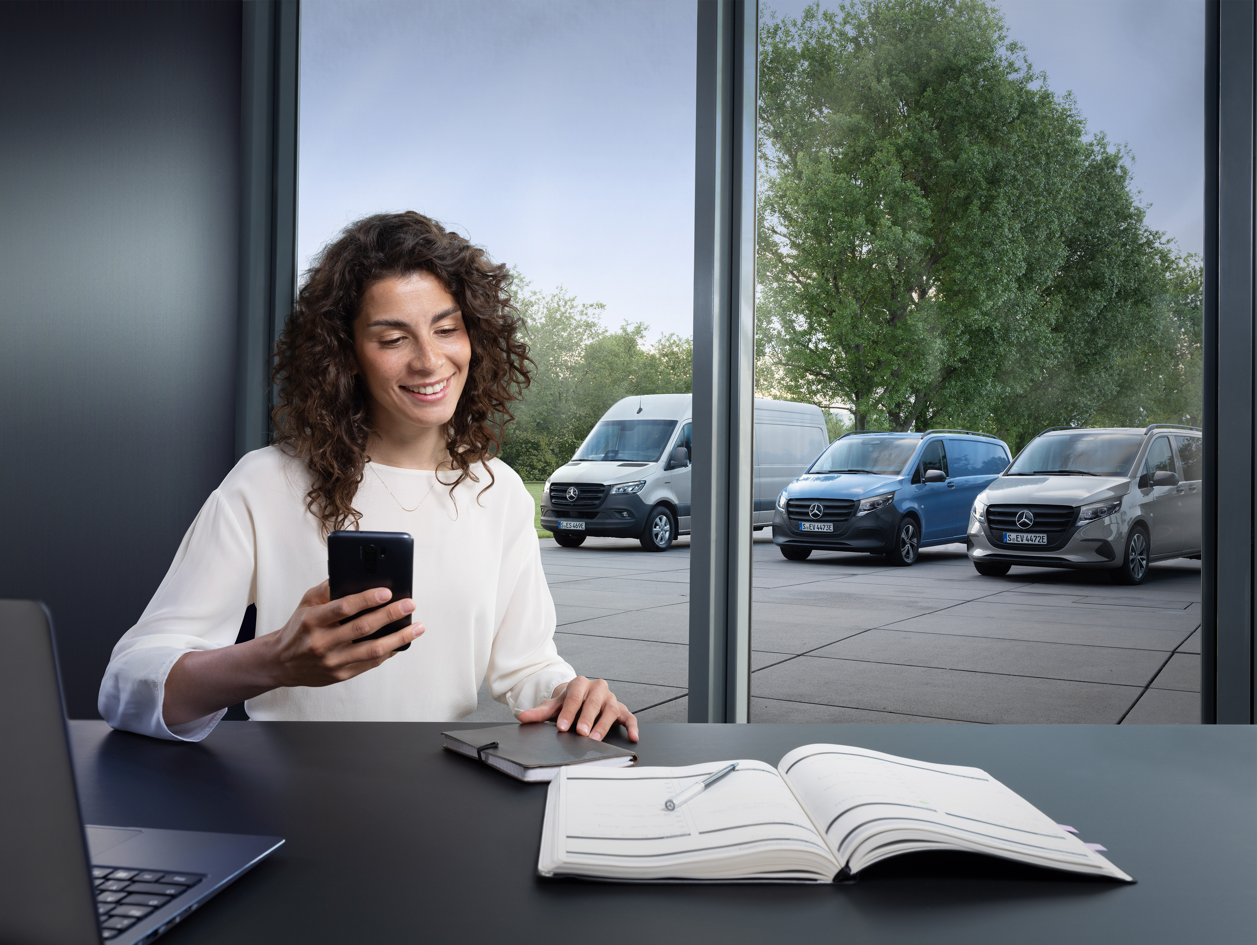 Mercedes-Benz | Confort | Prise de rendez-vous en ligne Femme avec smartphone devant des utilitaires Mercedes-Benz.