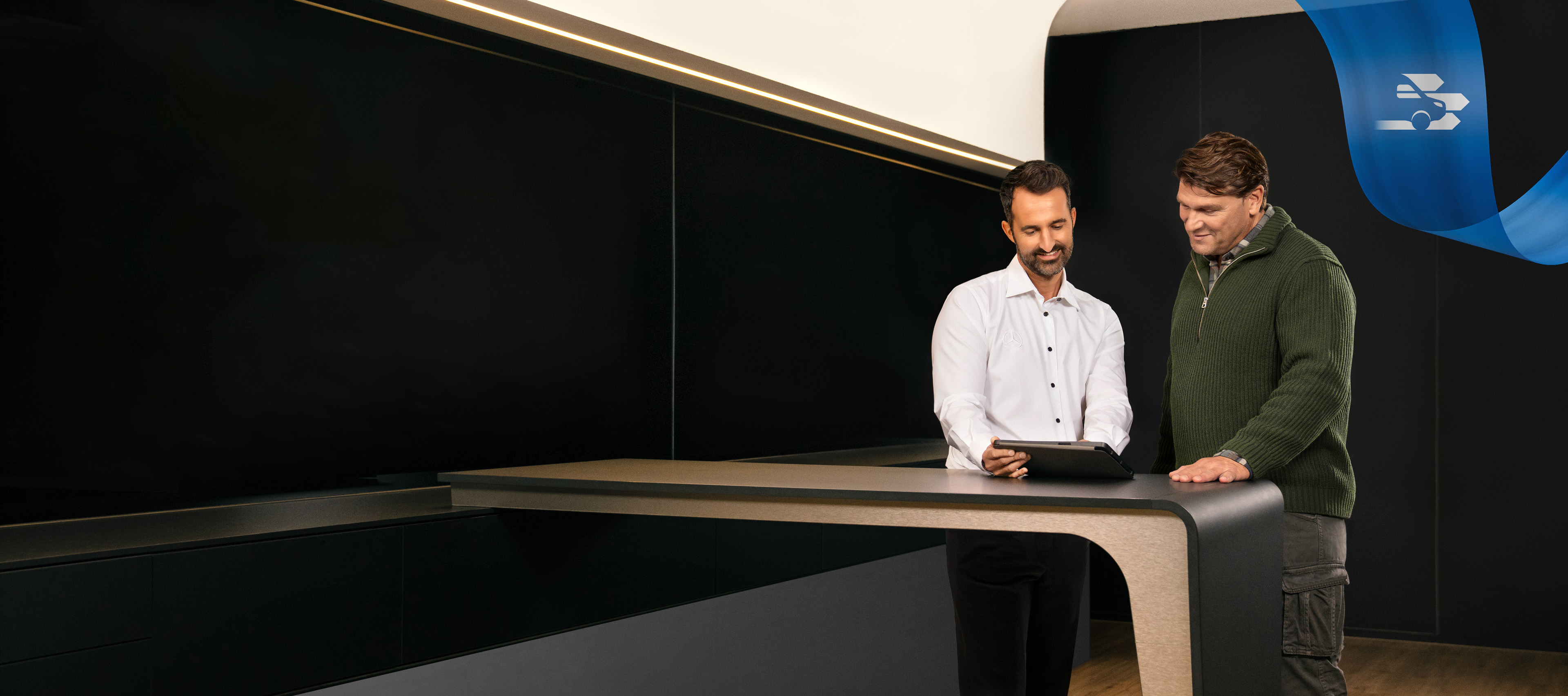 Mercedes-Benz | Convenience | Partner di assistenza Due uomini in piedi nell'ufficio di un partner di assistenza Mercedes-Benz mentre discutono di qualcosa visto su un tablet