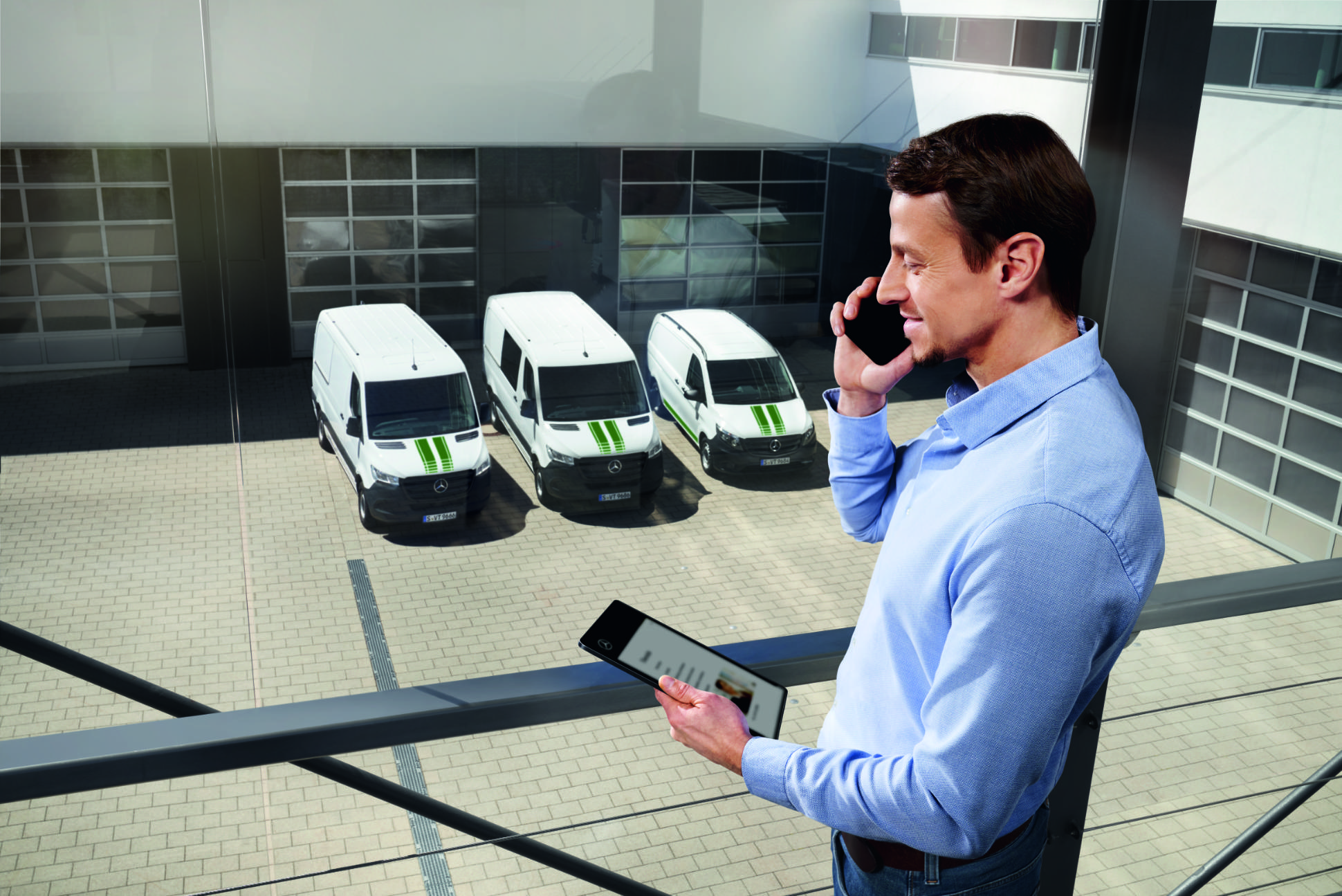 Van Uptime Monitor | Digital Extras | Mercedes-Benz A Mercedes-Benz consultant standing with a phone and a tablet in the hand with Mercedes-Benz Transporters in the background.