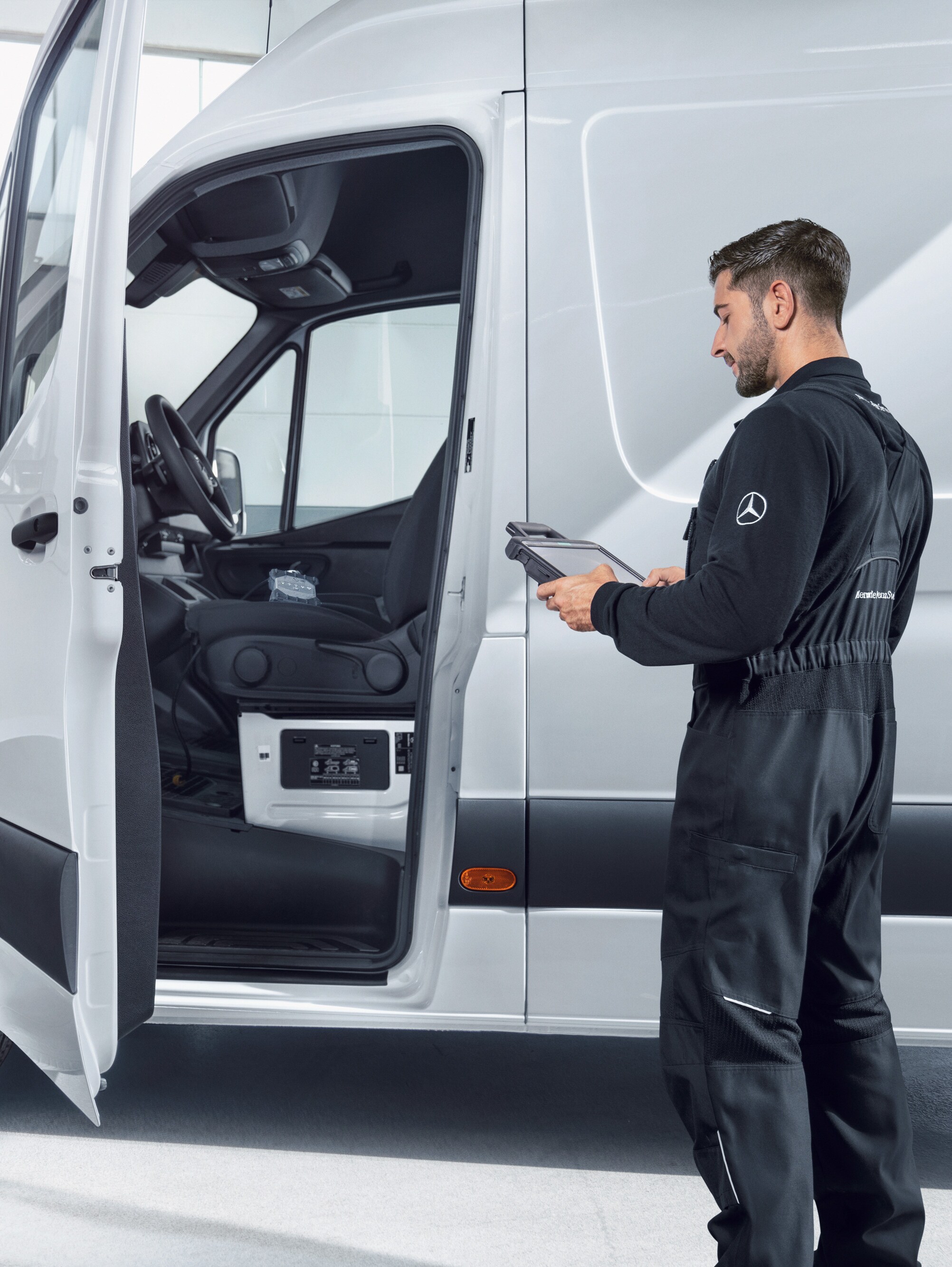 Mécanicien contrôlant un utilitaire Mercedes-Benz blanc avec une tablette.