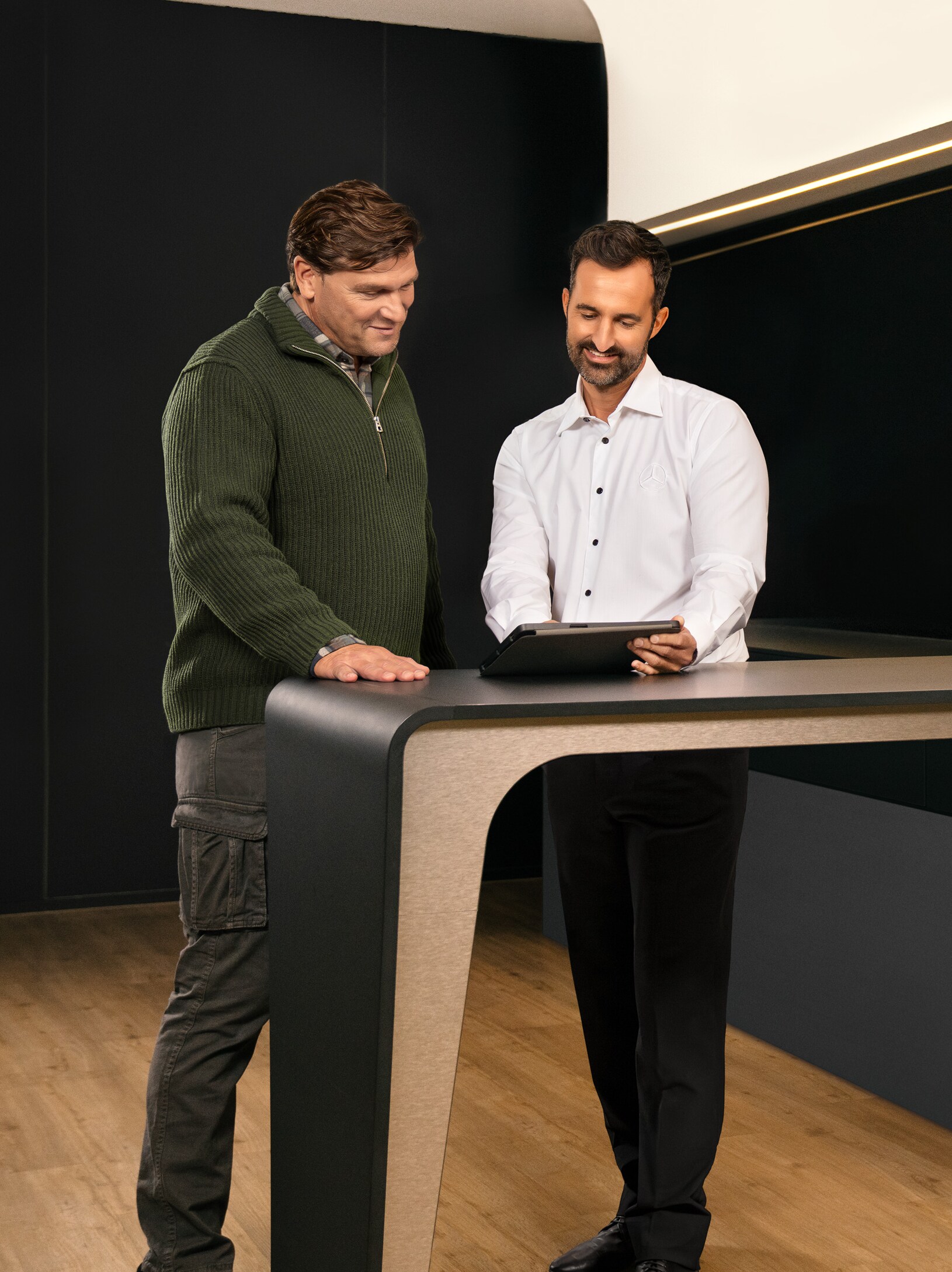 Zwei Männer, die sich beraten, stehen um einen Tisch herum und schauen auf ein iPad.