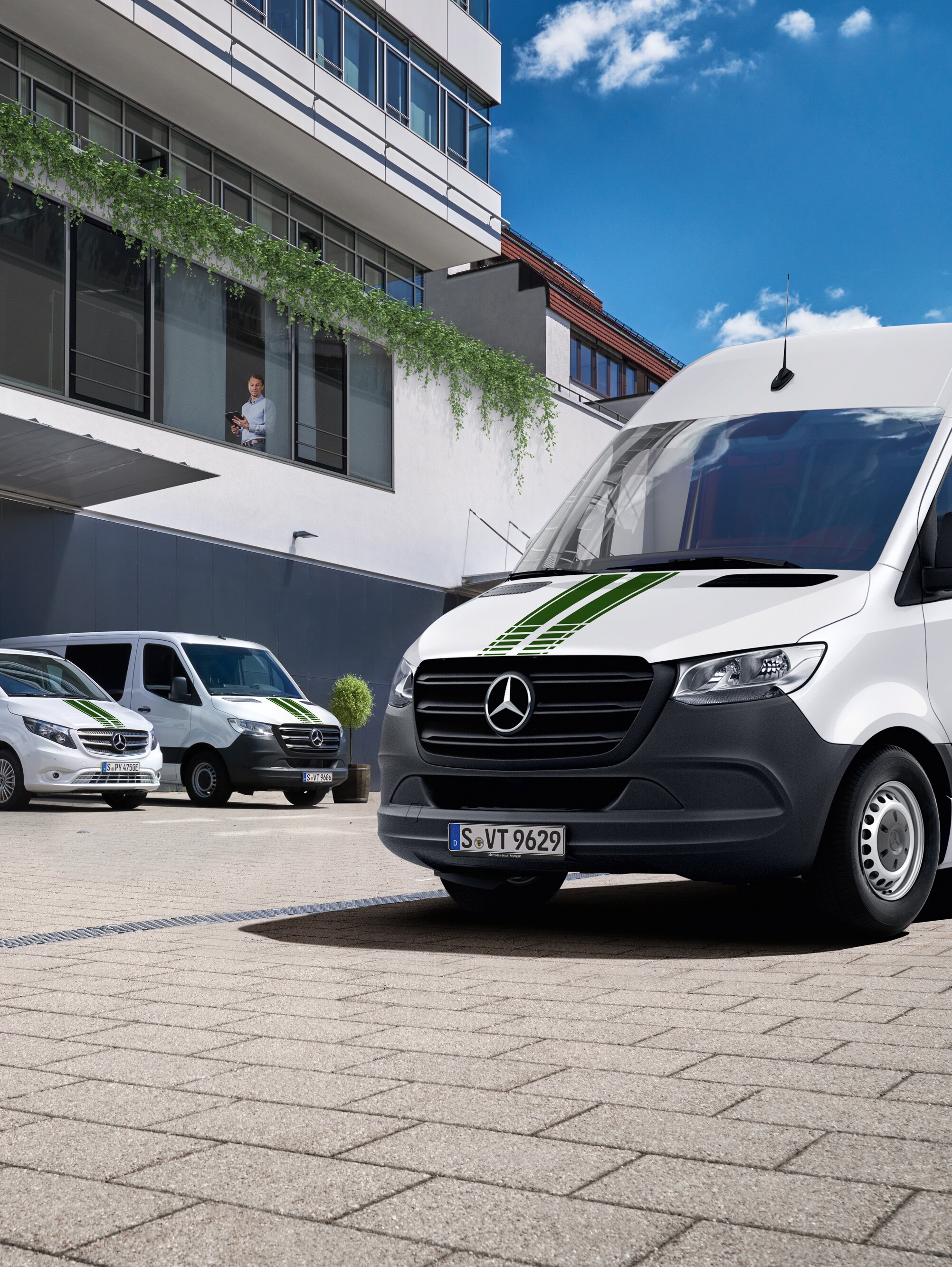 Una flotta di veicoli commerciali Mercedes-Benz bianchi davanti a un edificio per uffici in una giornata di sole con cielo azzurro.