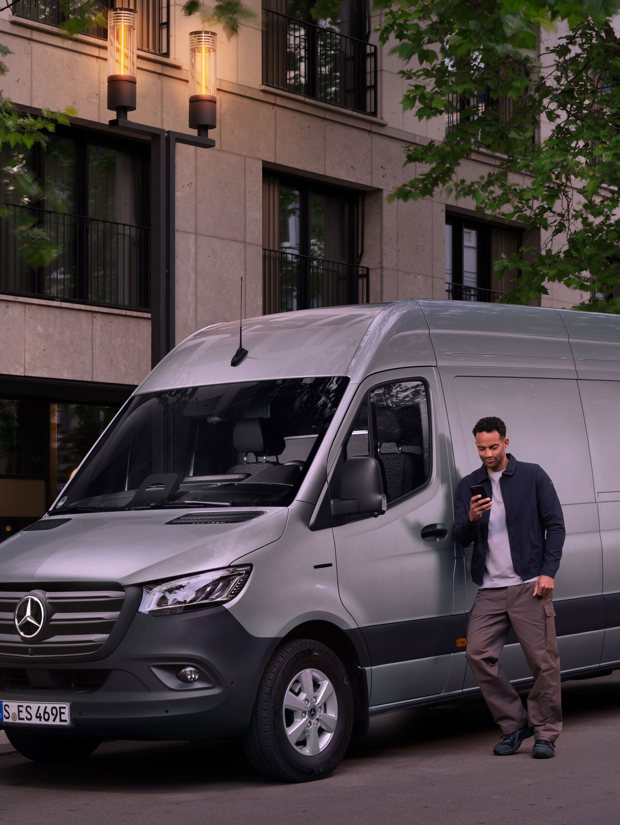 Un homme s'appuie sur une Mercedes-Benz Sprinter couleur argent et remplit un rapport de dommages sur son téléphone portable.
