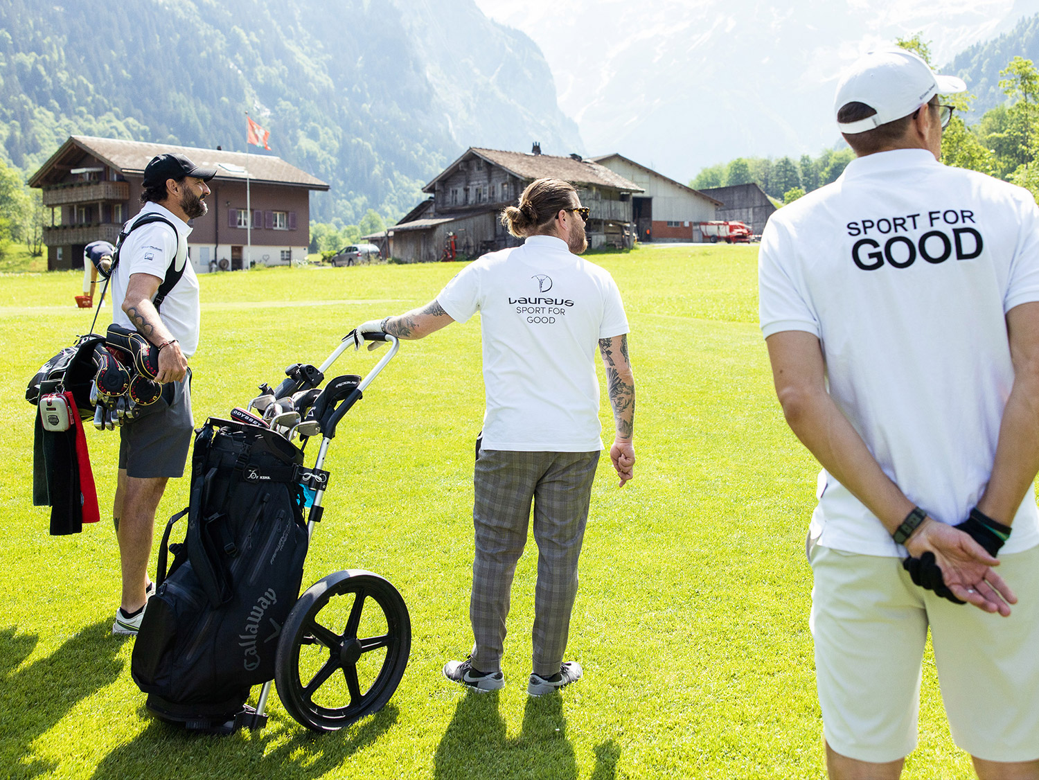 Sports for Good Day Tre golfisti stanno in piedi con le loro borse da golf sul prato e guardano oltre il campo.