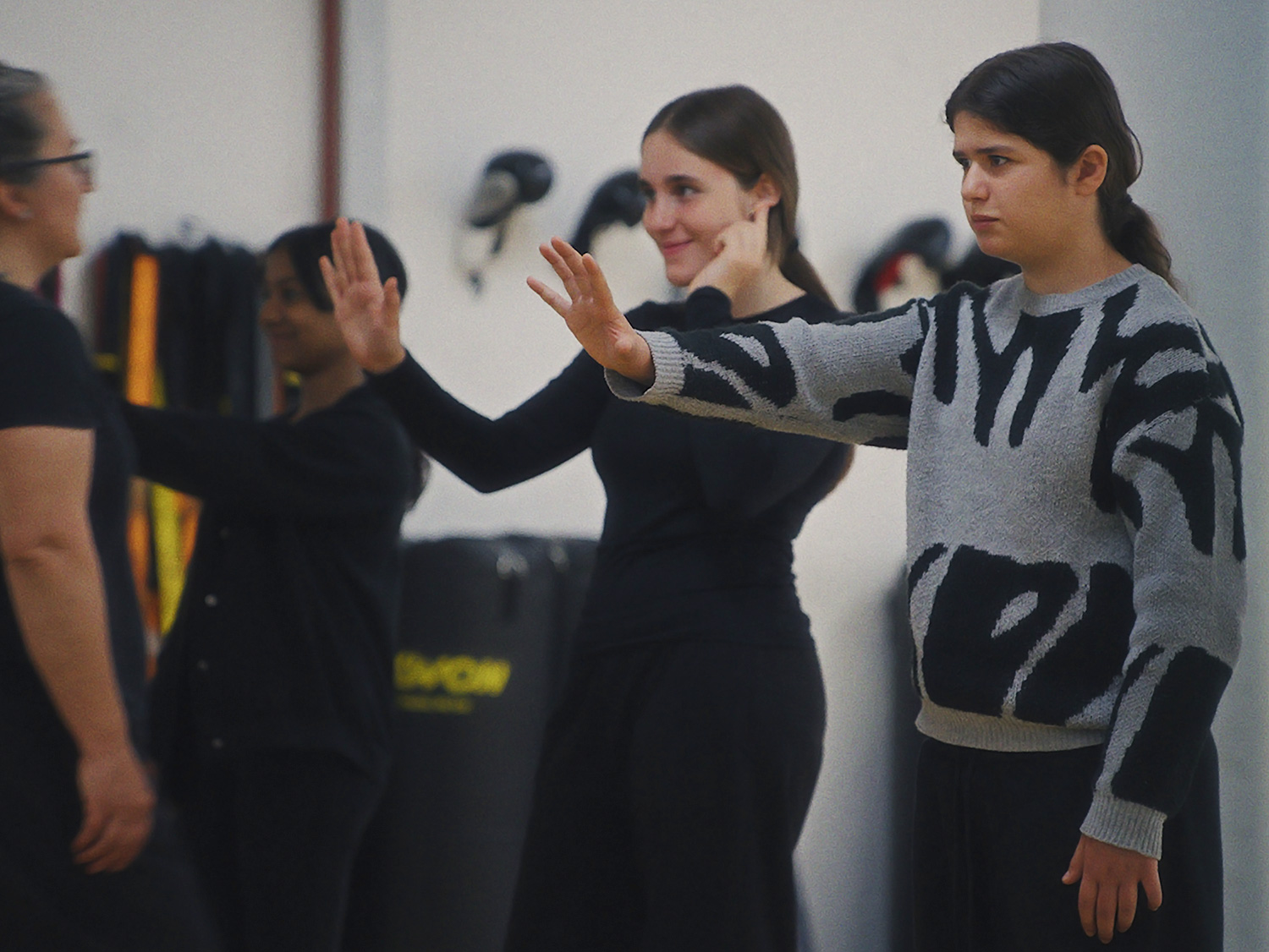 Engagement Laureus Deux adolescentes lèvent les bras pour se protéger, en position de défense, tandis que, derrière elles, l’entraîneuse observe attentivement la scène.