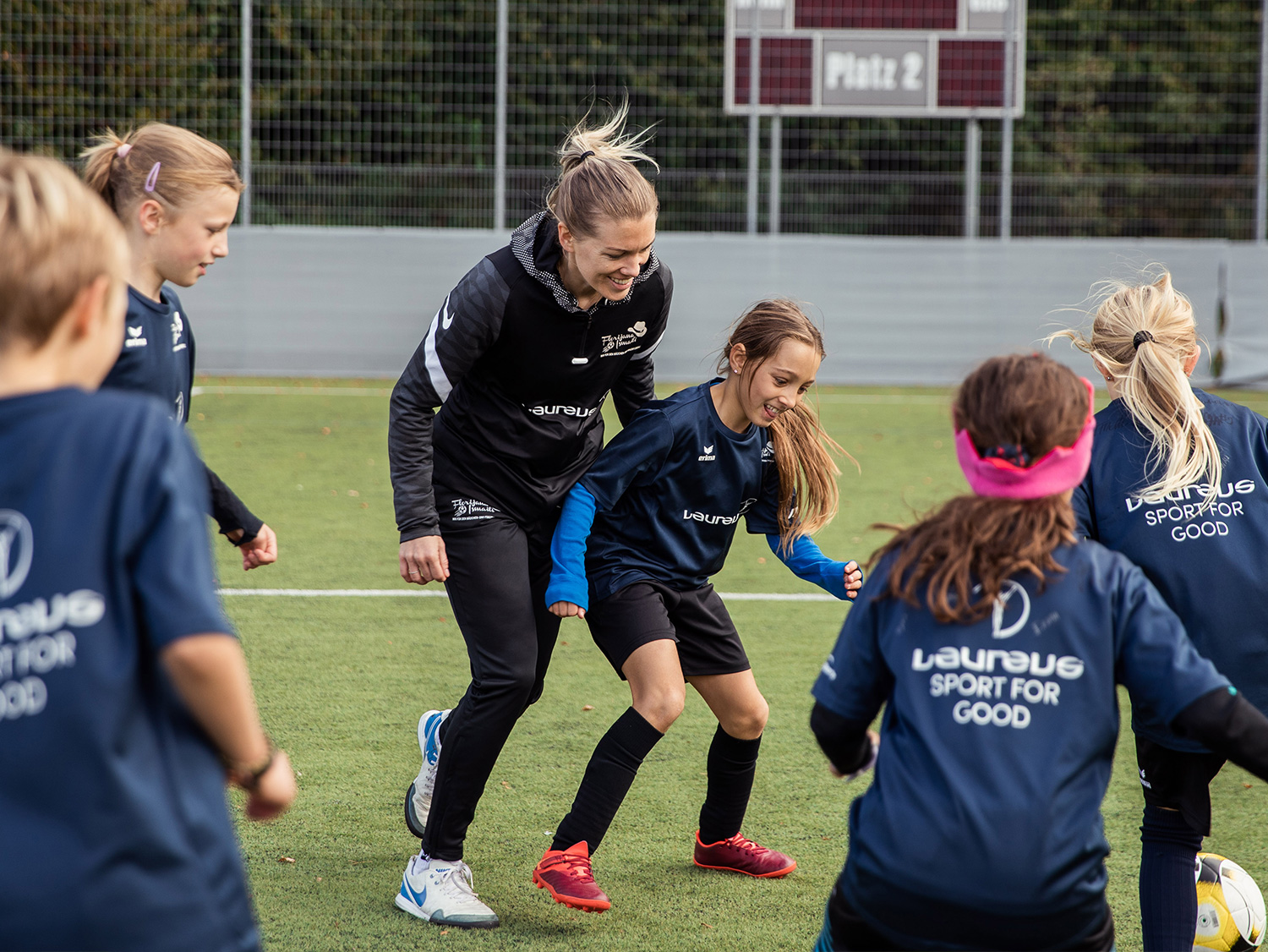 Laureus Sport for Good Kinder jagen gemeinsam mit ihrer Trainerin dem Ball über das Fussballfeld hinterher.