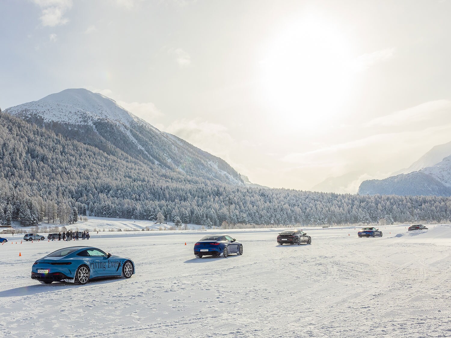 Divers véhicules Mercedes-Benz s’élancent sur une piste enneigée devant des forêts recouvertes de neige sous un soleil hivernal.
