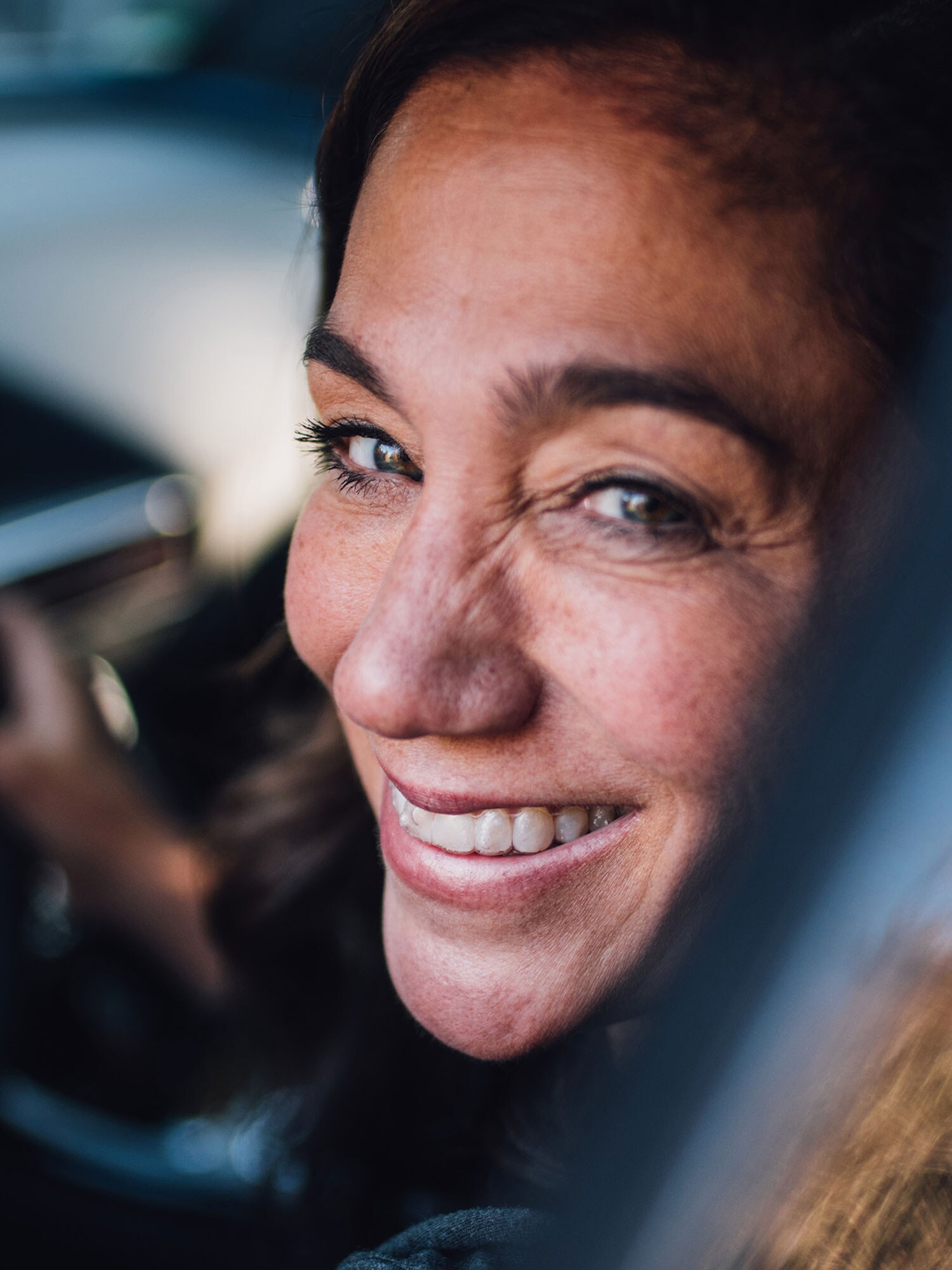 Femme souriante au volant d’une Mercedes, vue par la porte conducteur ouverte.