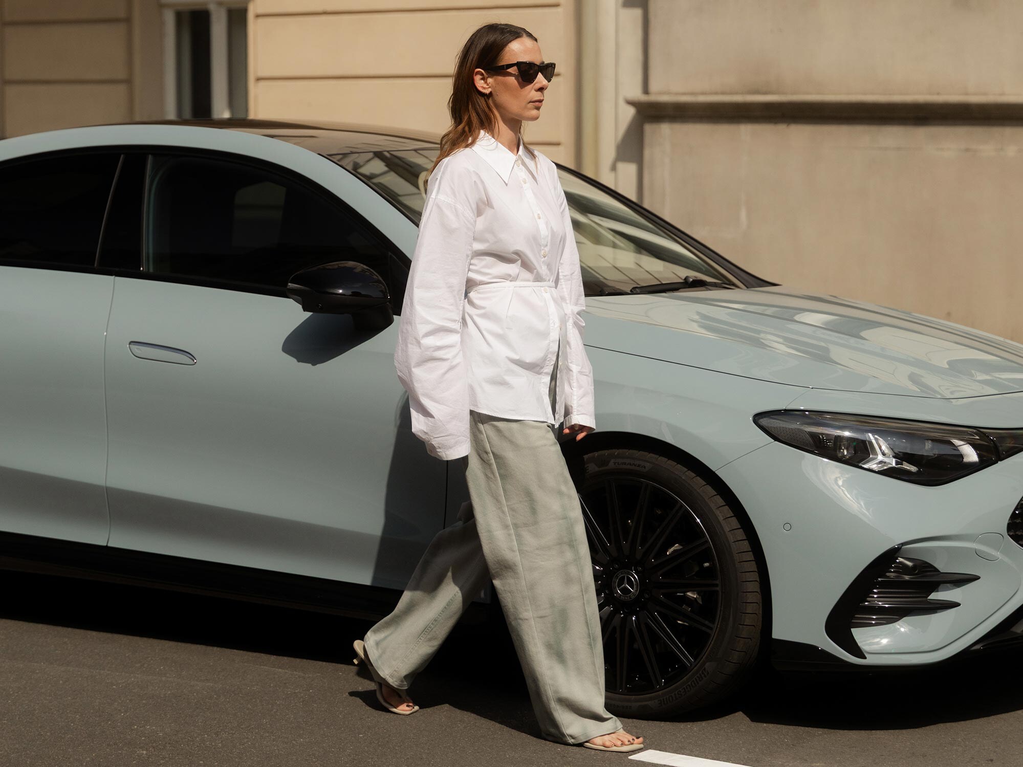 Femme élégante à côté d’une Mercedes-Benz grise.