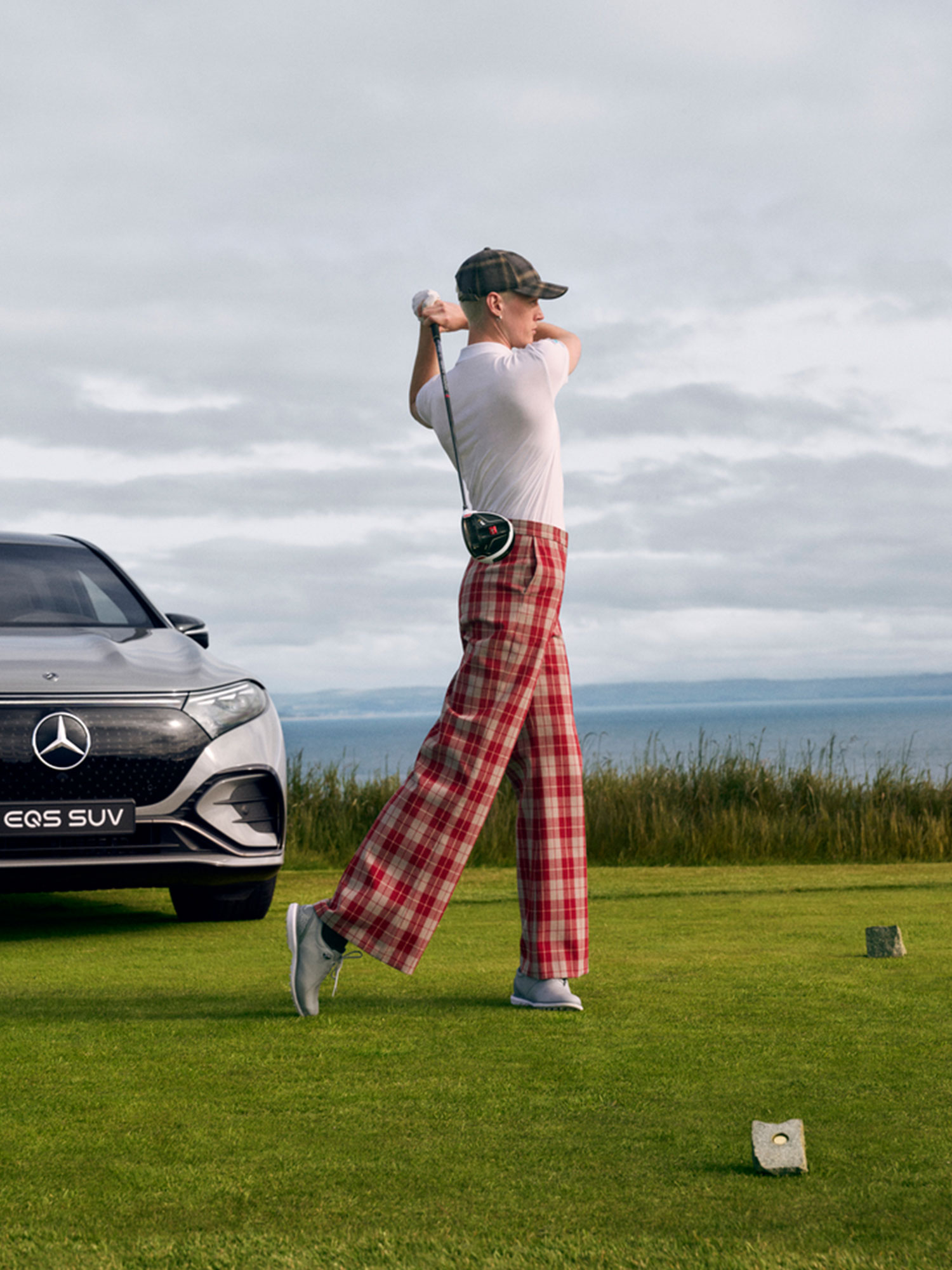 MercedesTrophy-Qualifikationsturniere Ein Golfer ist unmittelbar nach dem Abschlag in der typischen Schwungposition zu sehen. Im Hintergrund ist der Mercedes-Benz EQS SUV zu sehen.