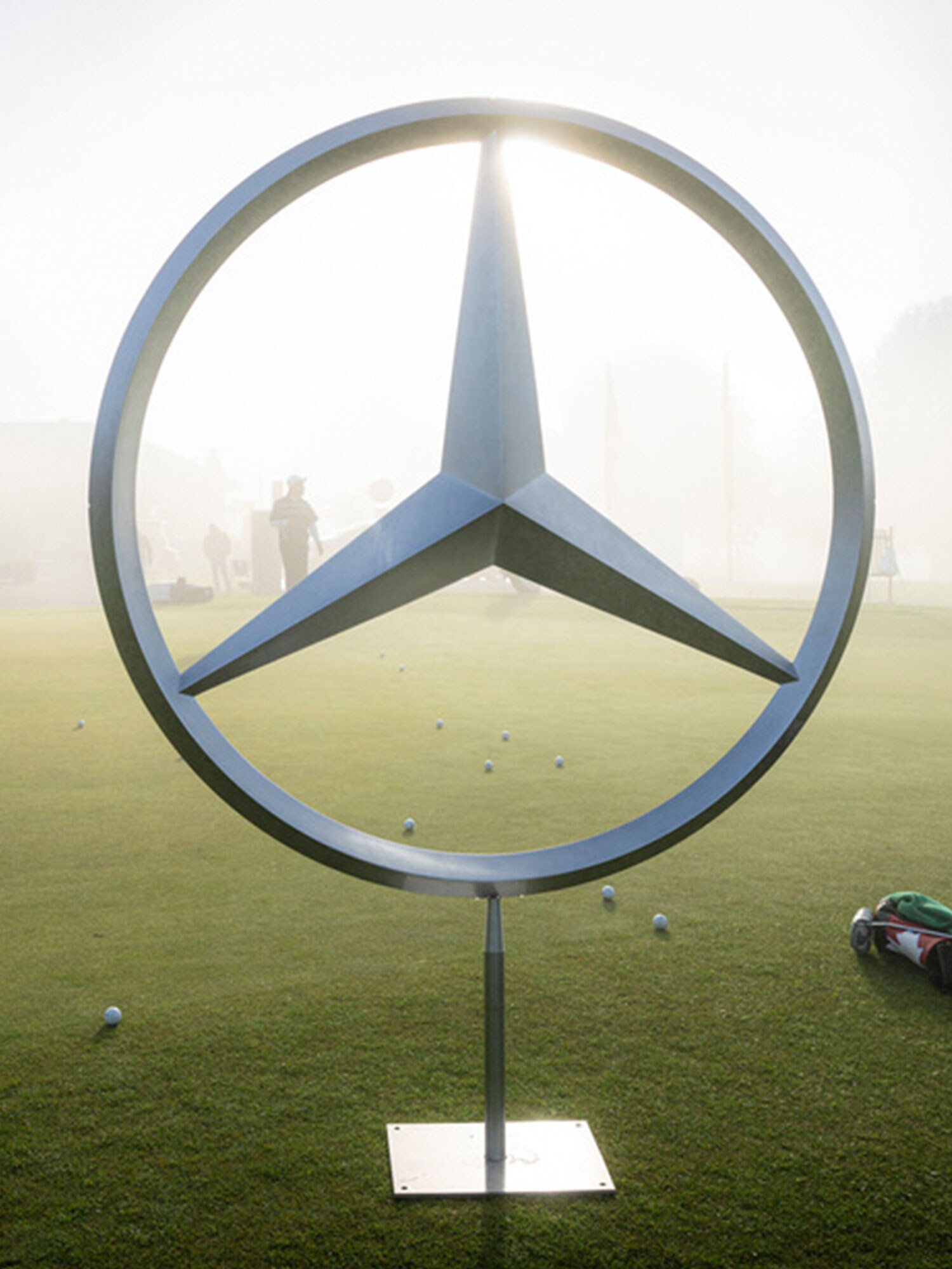 Une étoile Mercedes-Benz en métal sur un parcours de golf par temps brumeux et ensoleillé.