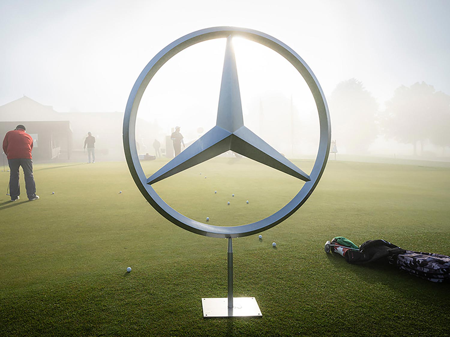 Mercedes-Benz Stern Mercedes-Benz Stern aus Metall auf einem Golfplatz bei Nebel und Sonnenschein.