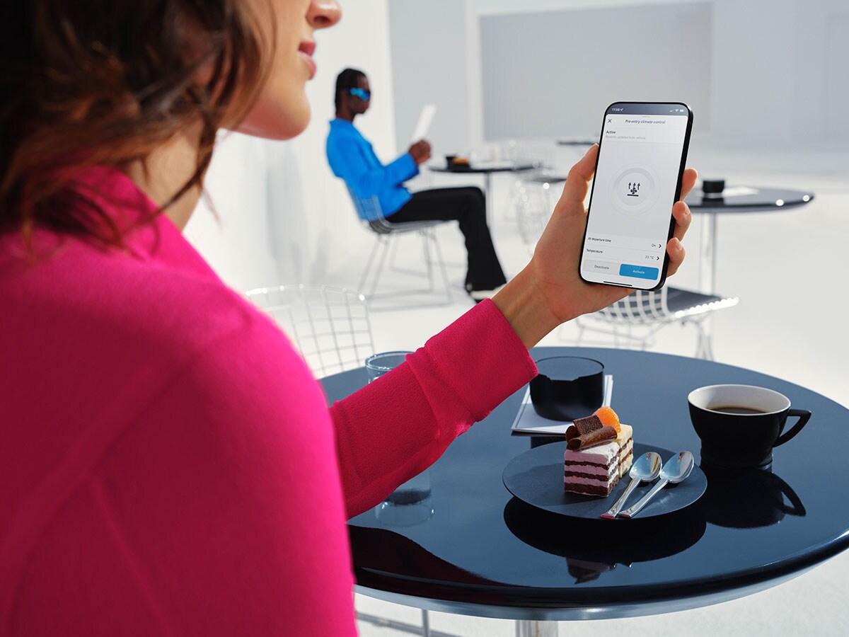 Eine Frau aktiviert in der Mercedes-Benz App die Vorklimatisierung ihres Elektroautos. 