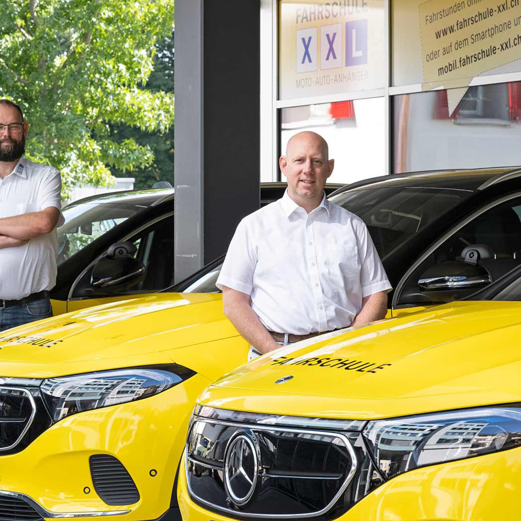 Drei Männer vor gelben, elektrischen Mercedes-Benz Fahrschulautos