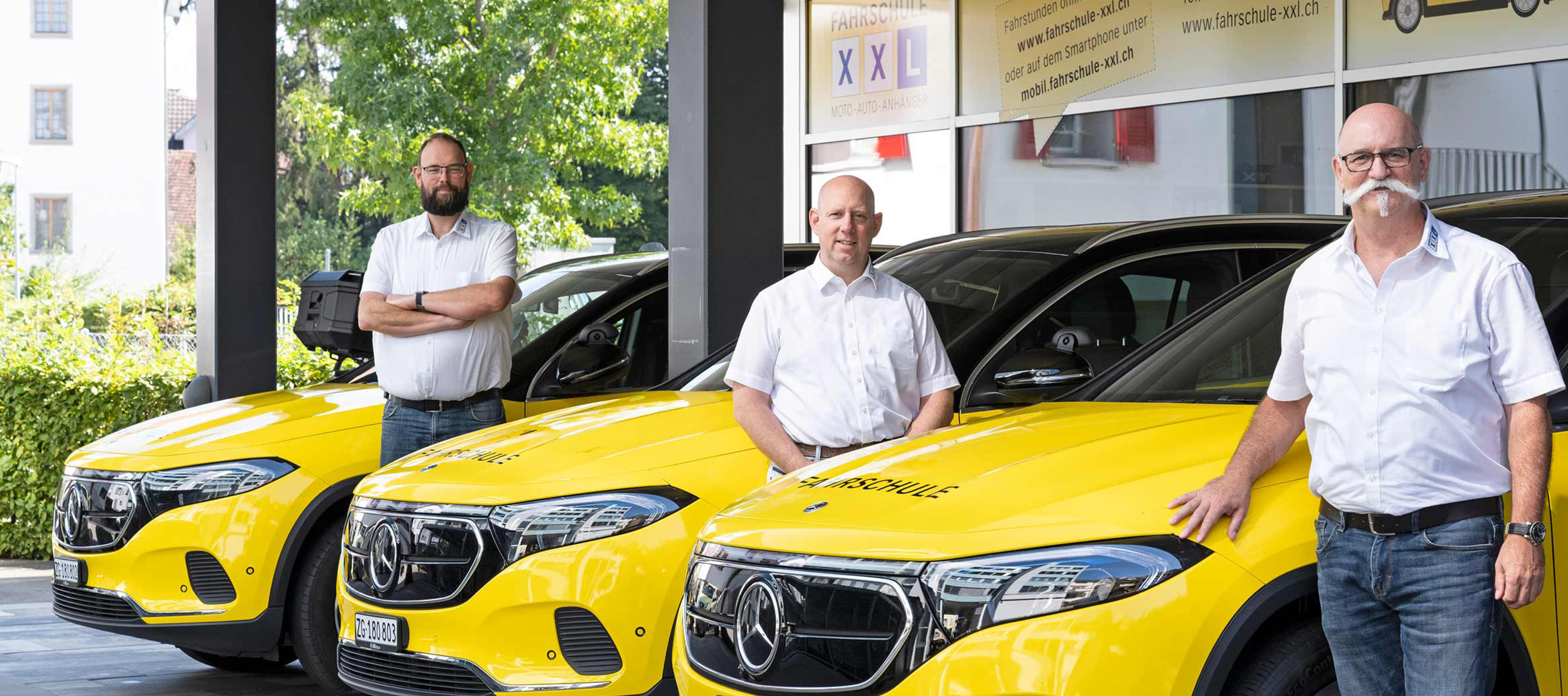 Die drei Fahrlehrer der Fahrschule XXL posieren vor ihren gelben Mercedes-EQ Fahrzeugen Drei Männer vor gelben, elektrischen Mercedes-Benz Fahrschulautos