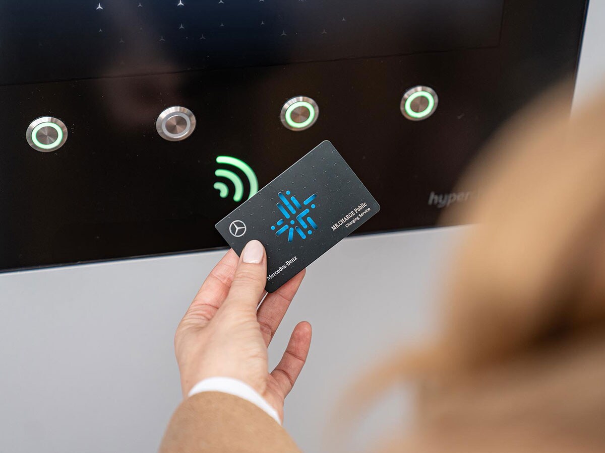 Une femme tient une carte de recharge MB.CHARGE Public devant un écran à une borne de recharge