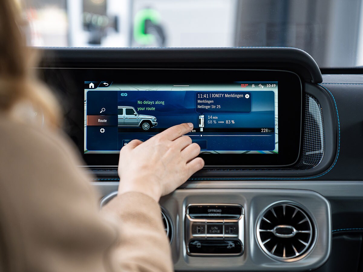 Frau bedient Navigationsdisplay eines Mercedes-Benz Elektroautos.