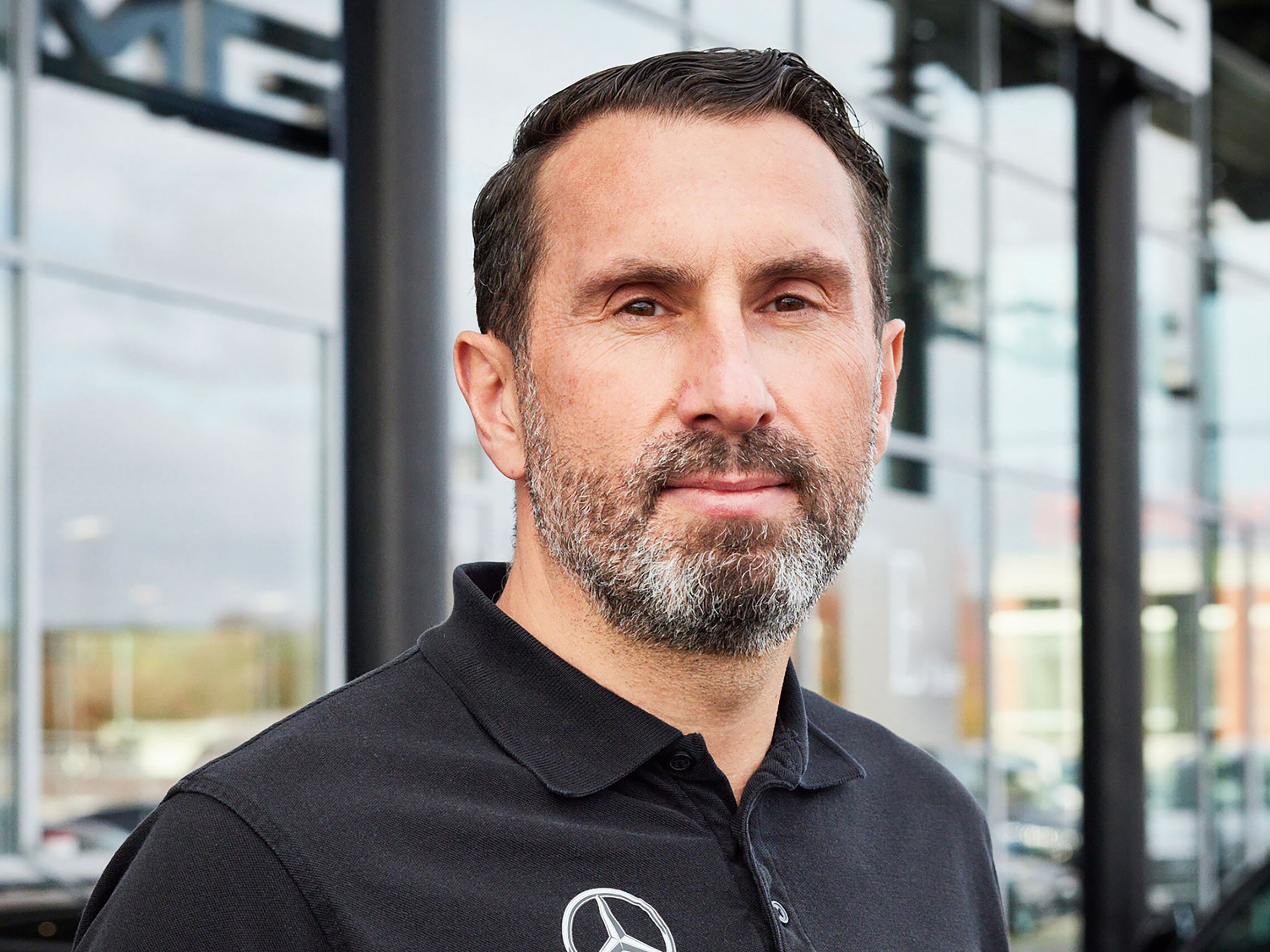 Automobilfachmann im Firmen-Poloshirt vor Gebäude eines Mercedes-Benz Partnerbetriebs 